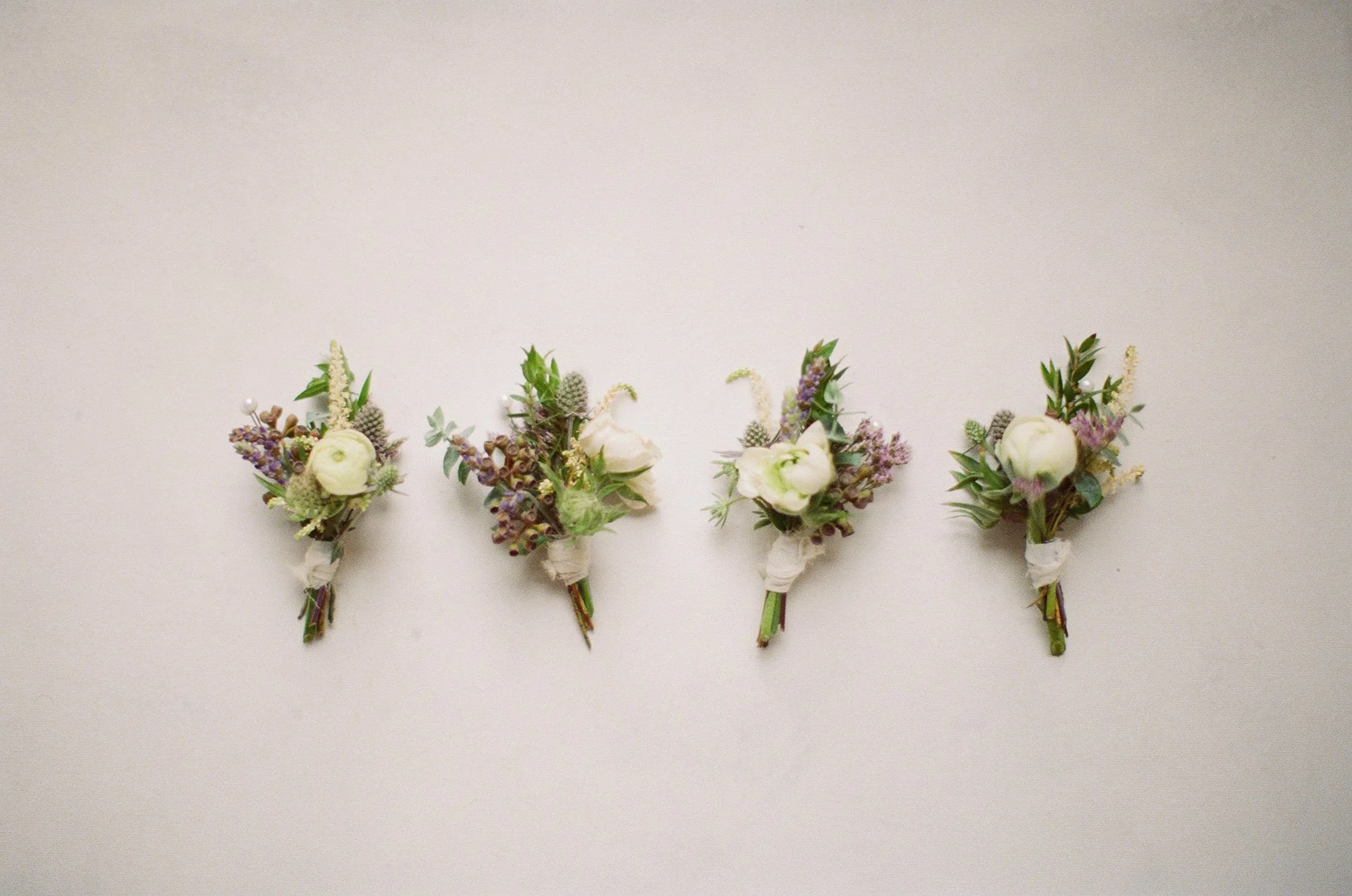 Wedding boutonnieres arranged on a white background at Cliffside Estate, photographed by Michael & Anna Costa