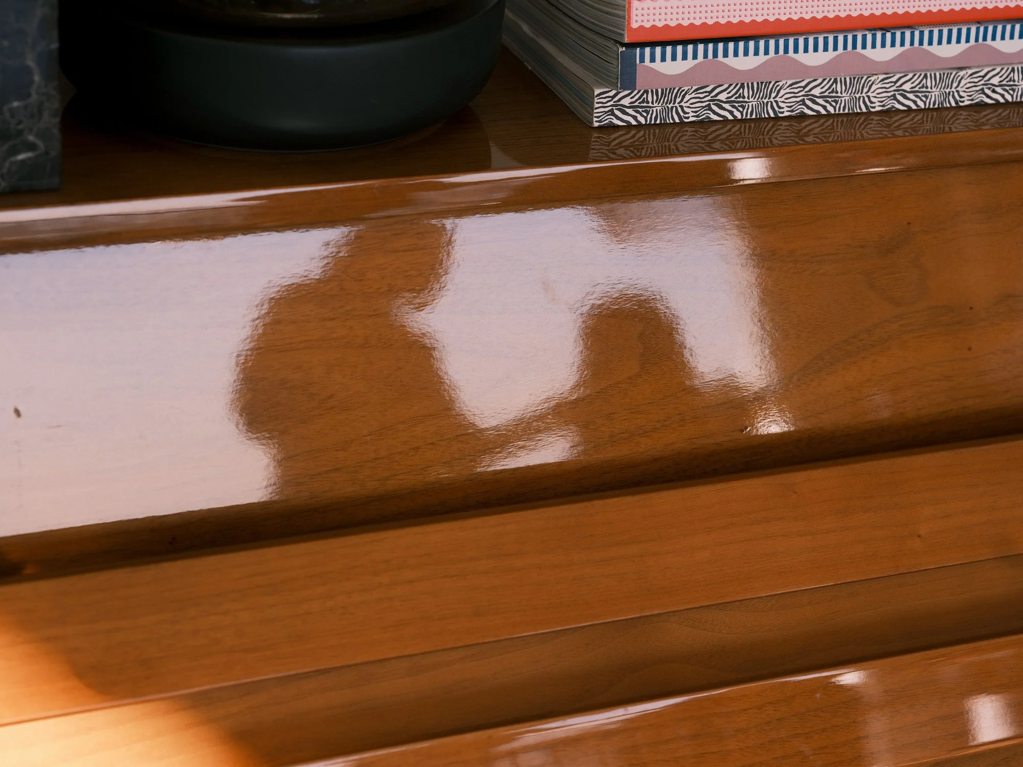 Reflection of two people on a polished wooden piano surface.