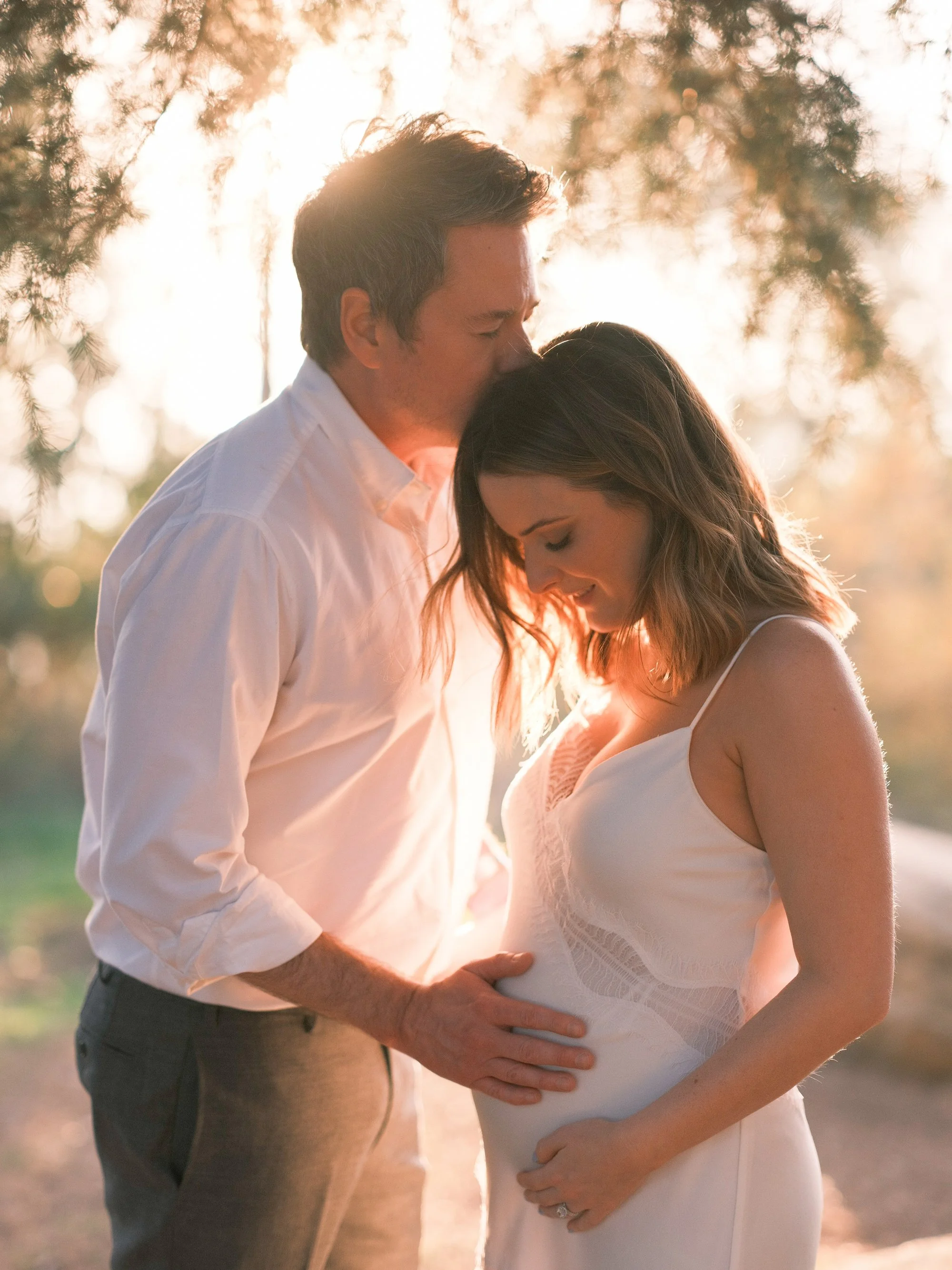Bride and groom embracing, standing close together in soft sunlight.