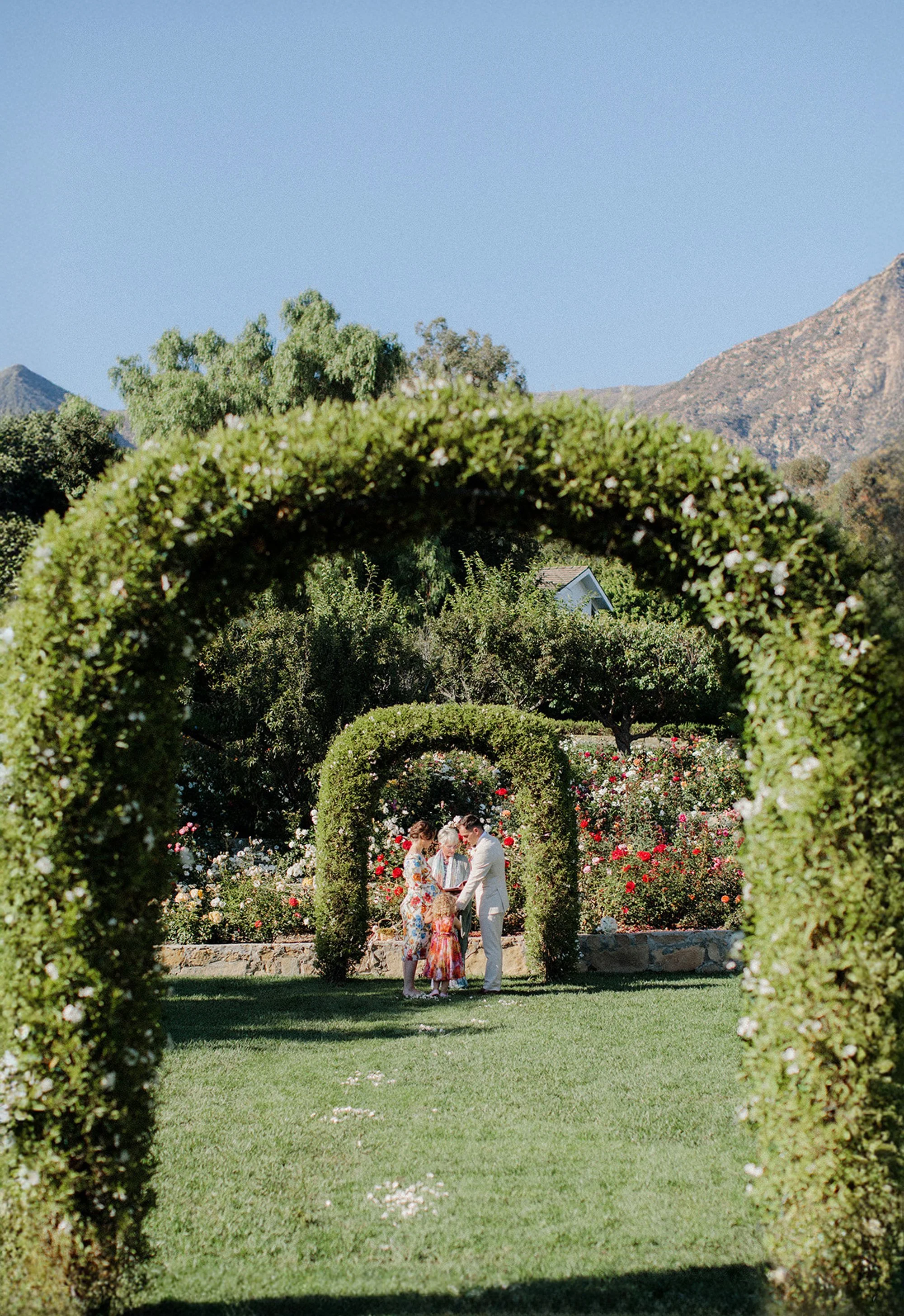 Family walking together under a green archway in a garden.