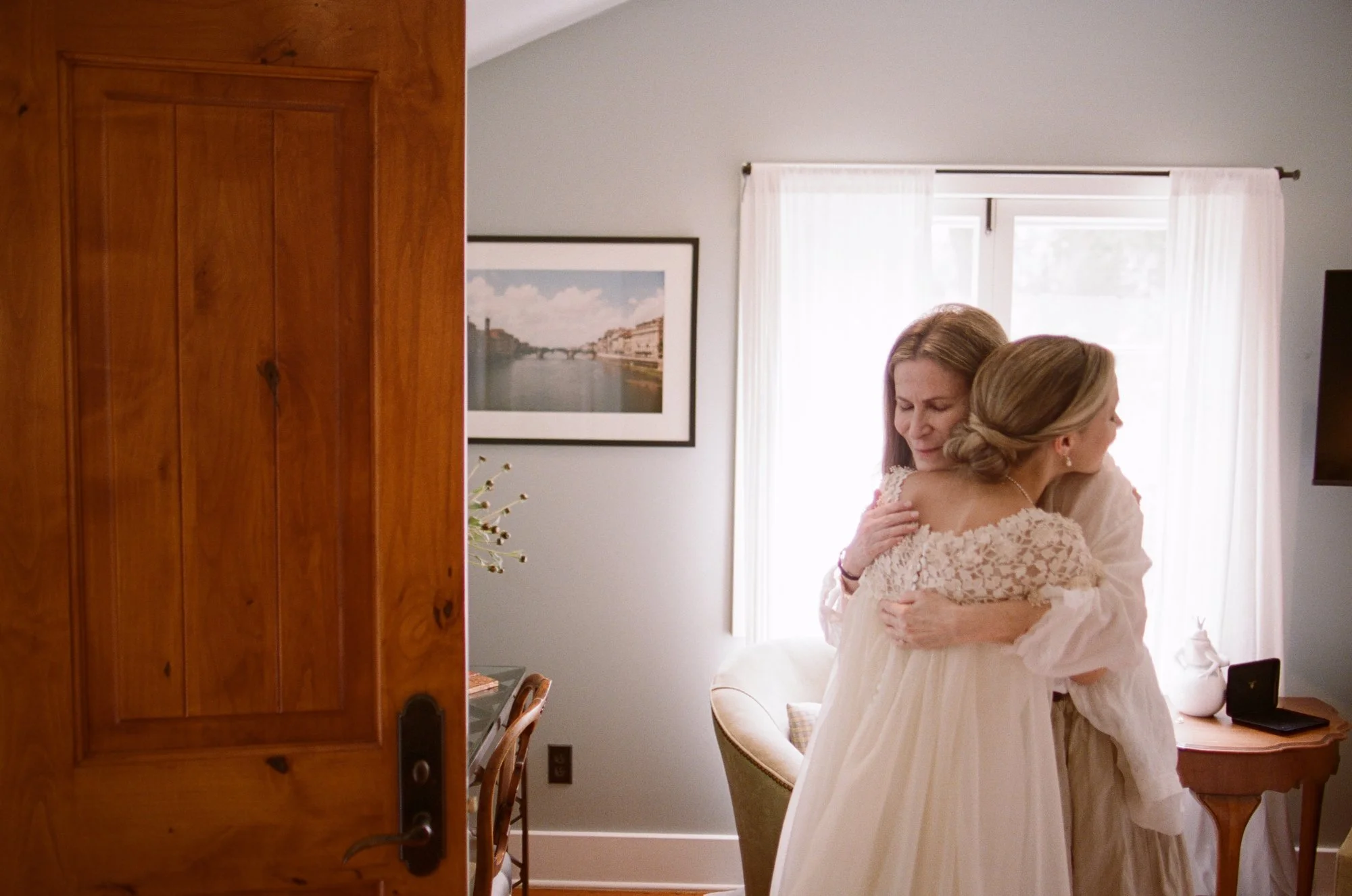 Bride hugging her mother in a warmly lit bedroom.