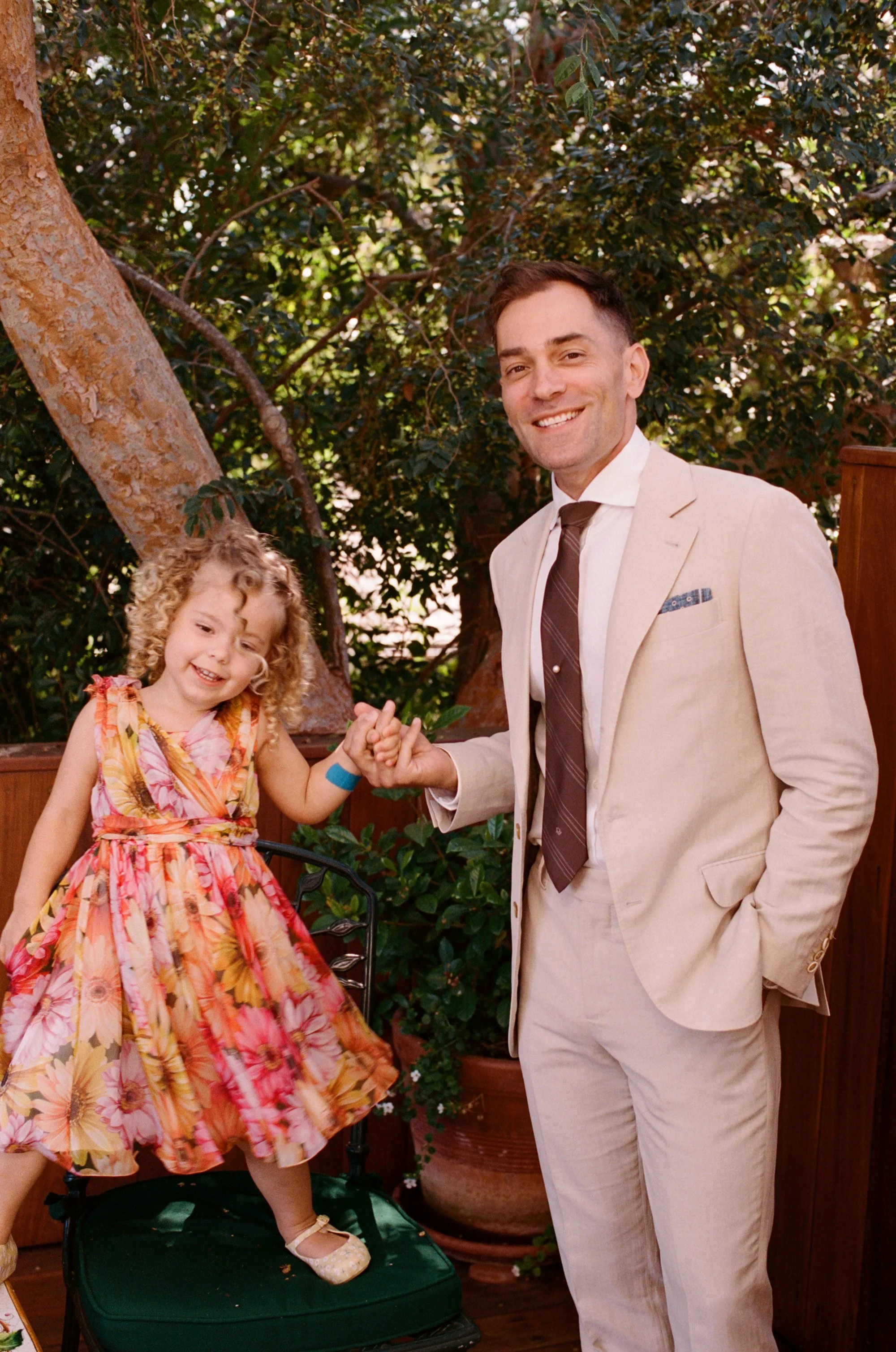Man in a suit and young girl in a colorful dress smiling together outdoors.
