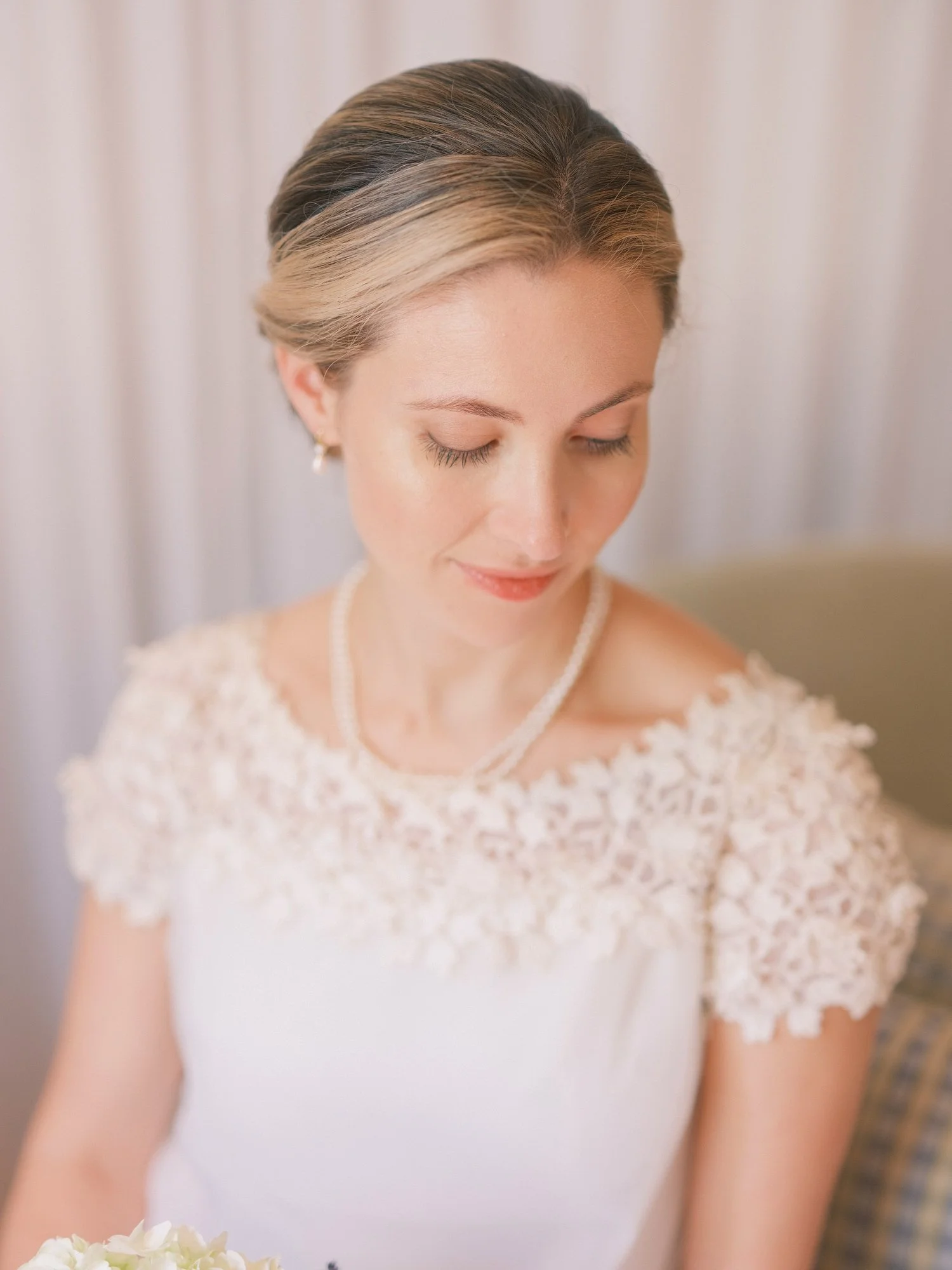 Bride with pearl-embellished lace dress, looking down with a soft expression.