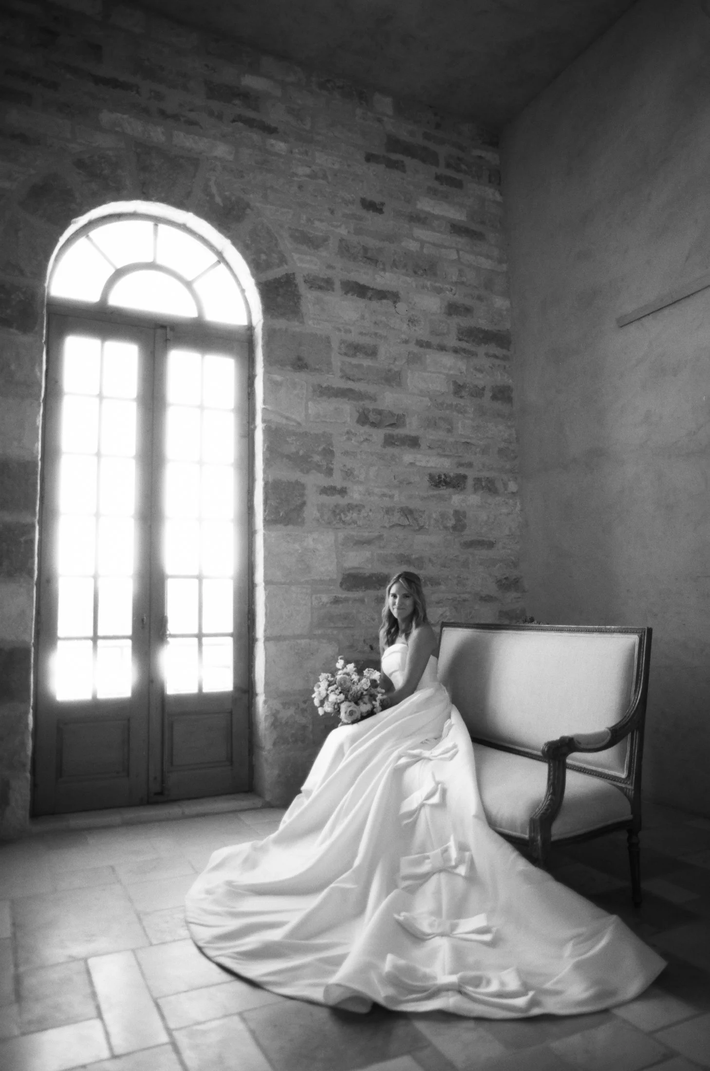 Bride in wedding dress sitting by arched window in bridal suite at Sunstone Villa, photographed by Michael & Anna Costa