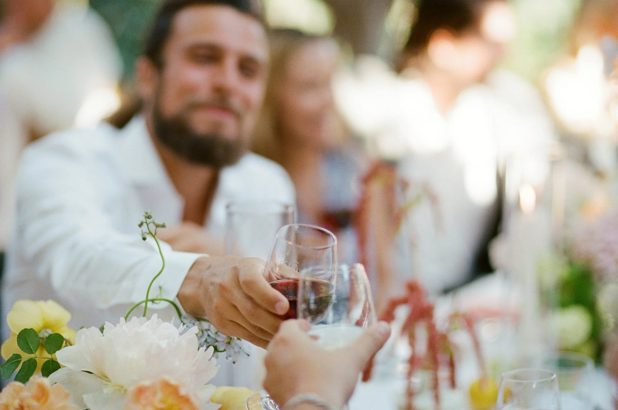 Guest raising a glass in a toast at outdoor wedding reception at San Ysidro Ranch, photographed by Michael & Anna Costa