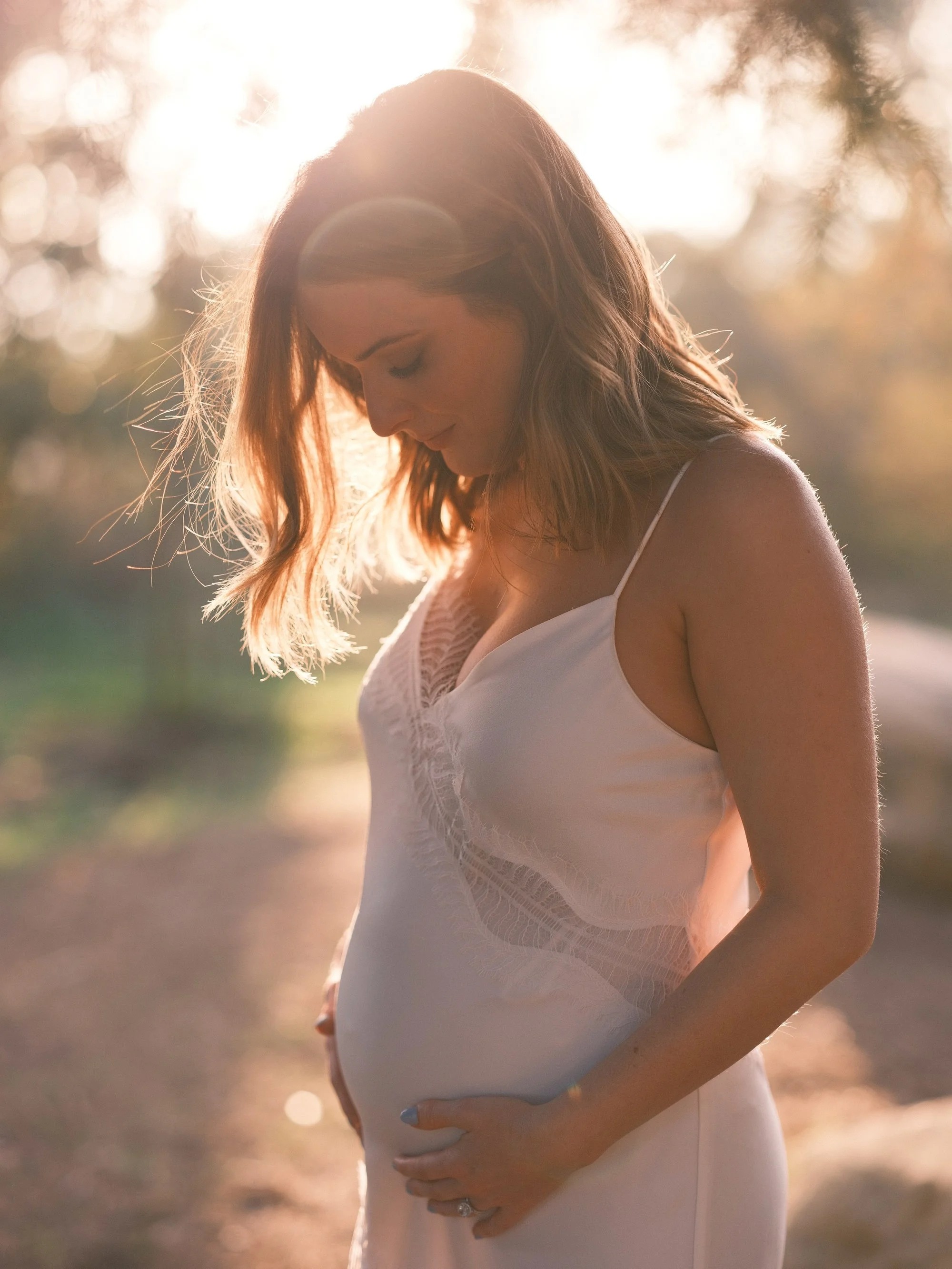 Bride in a white dress, standing alone in golden sunlight.
