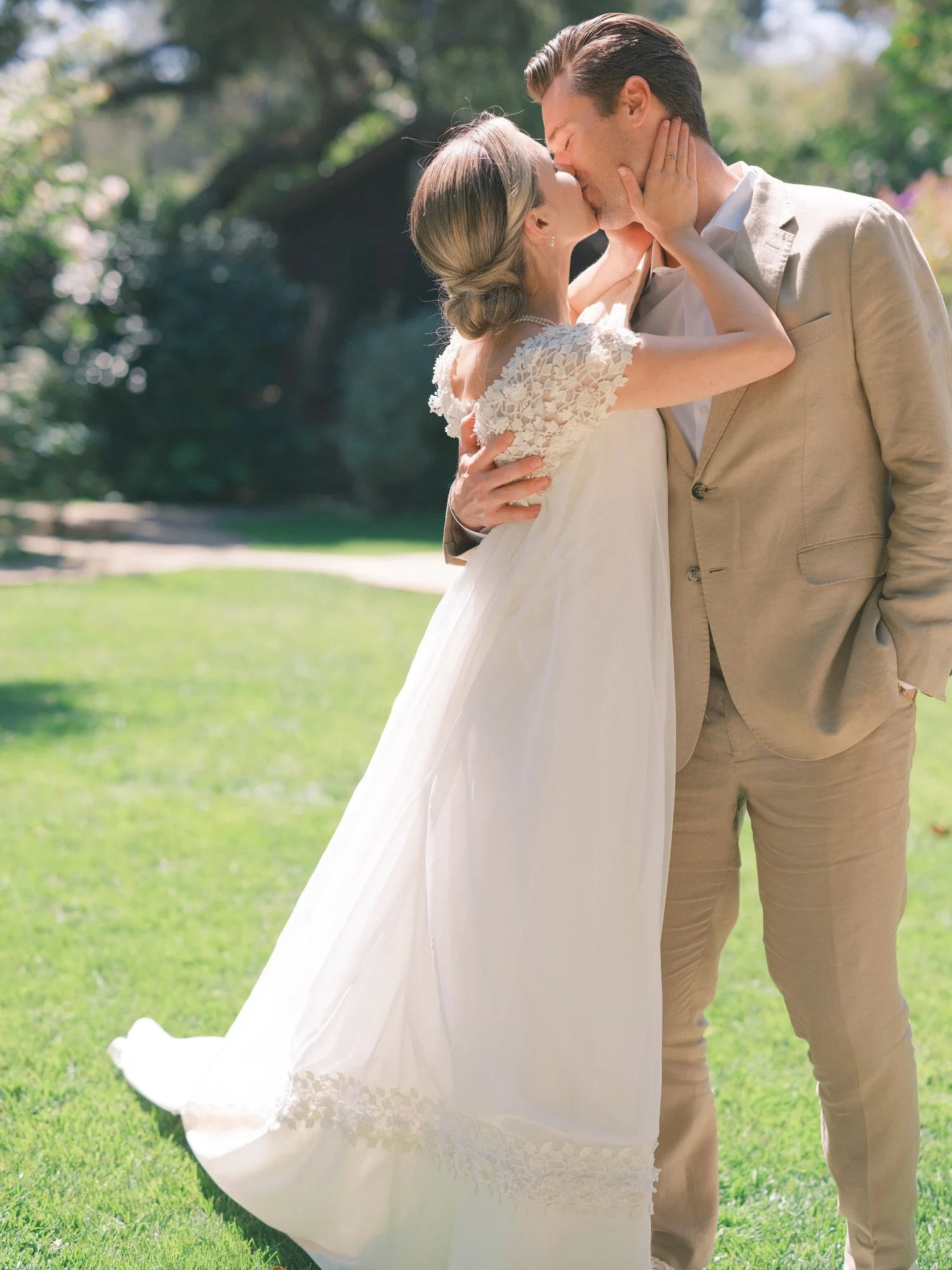 Bride and groom sharing a joyful embrace on a sunlit lawn.