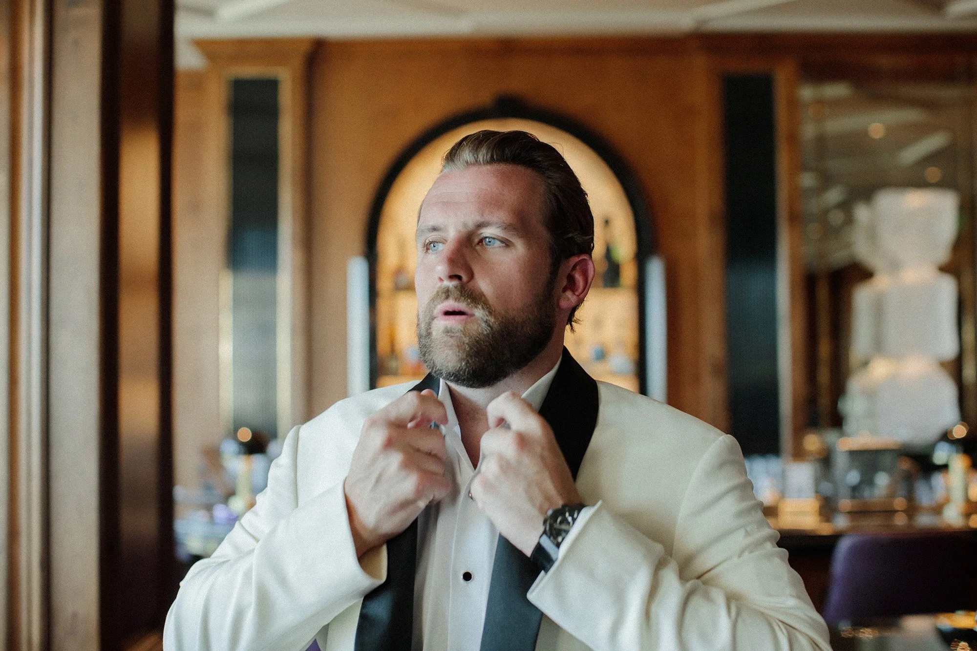 Groom adjusting bow tie while getting ready in a suite at Rosewood Miramar Beach wedding, photographed by Michael & Anna Costa