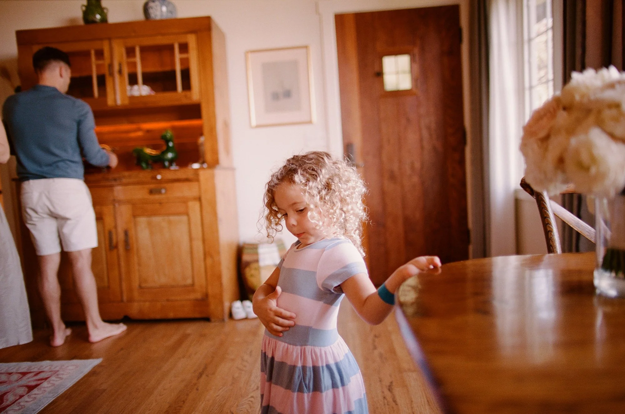 Young girl in a striped dress playing with a ribbon in a cozy kitchen.