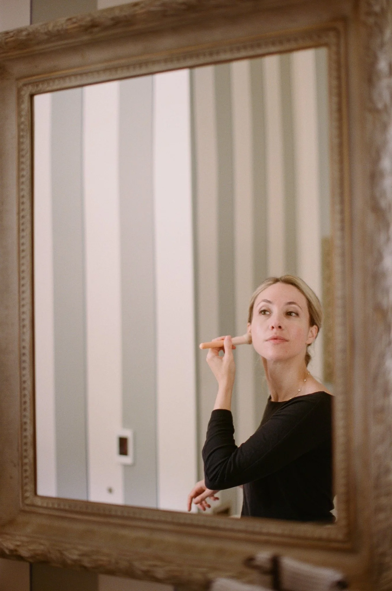 Woman in a black top looking in the mirror while adjusting her earring.