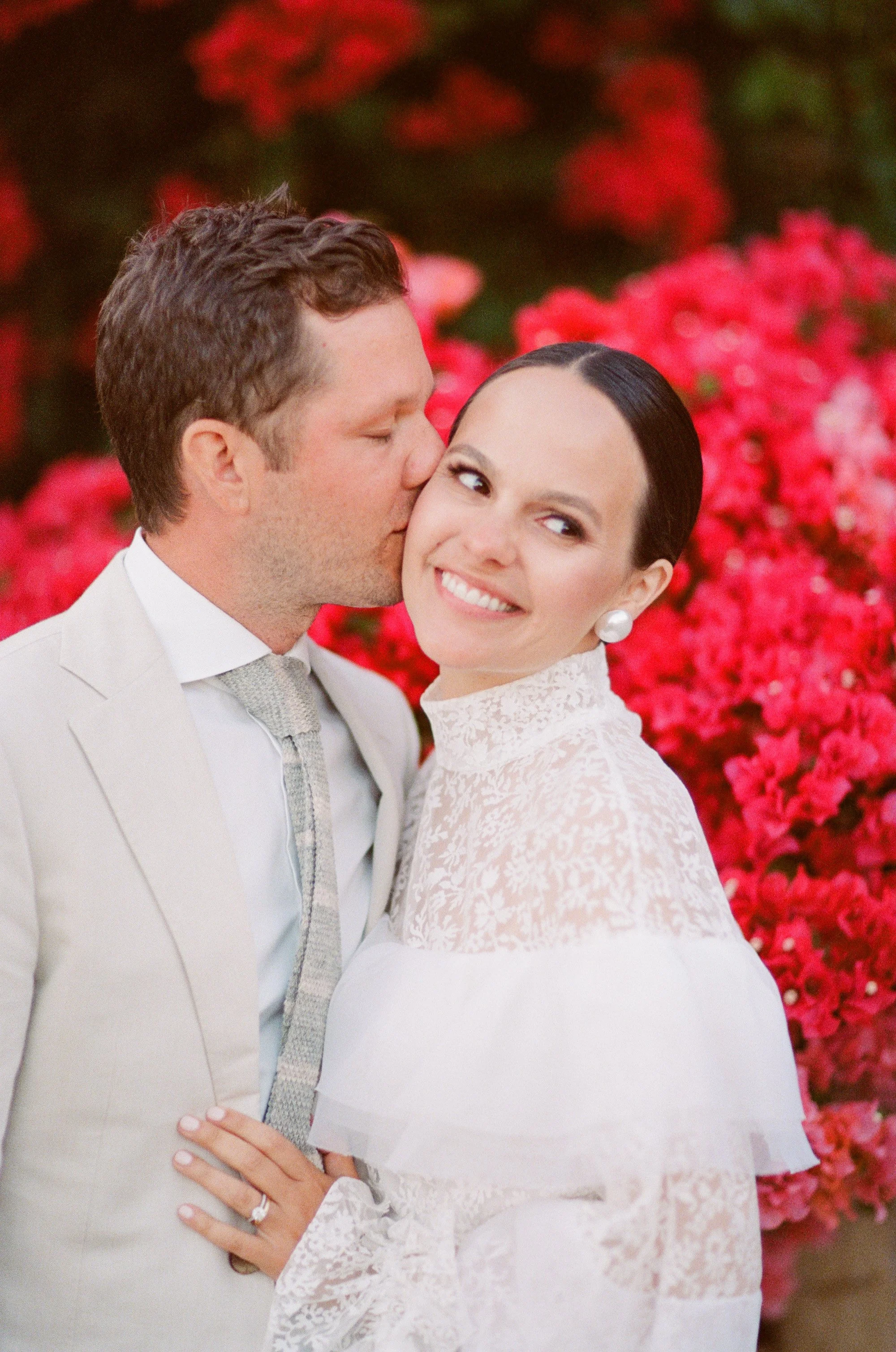 Bride and groom holding hands in front of a red and white bougainvillea wall at San Ysidro Ranch, photographed by Michael & Anna Costa