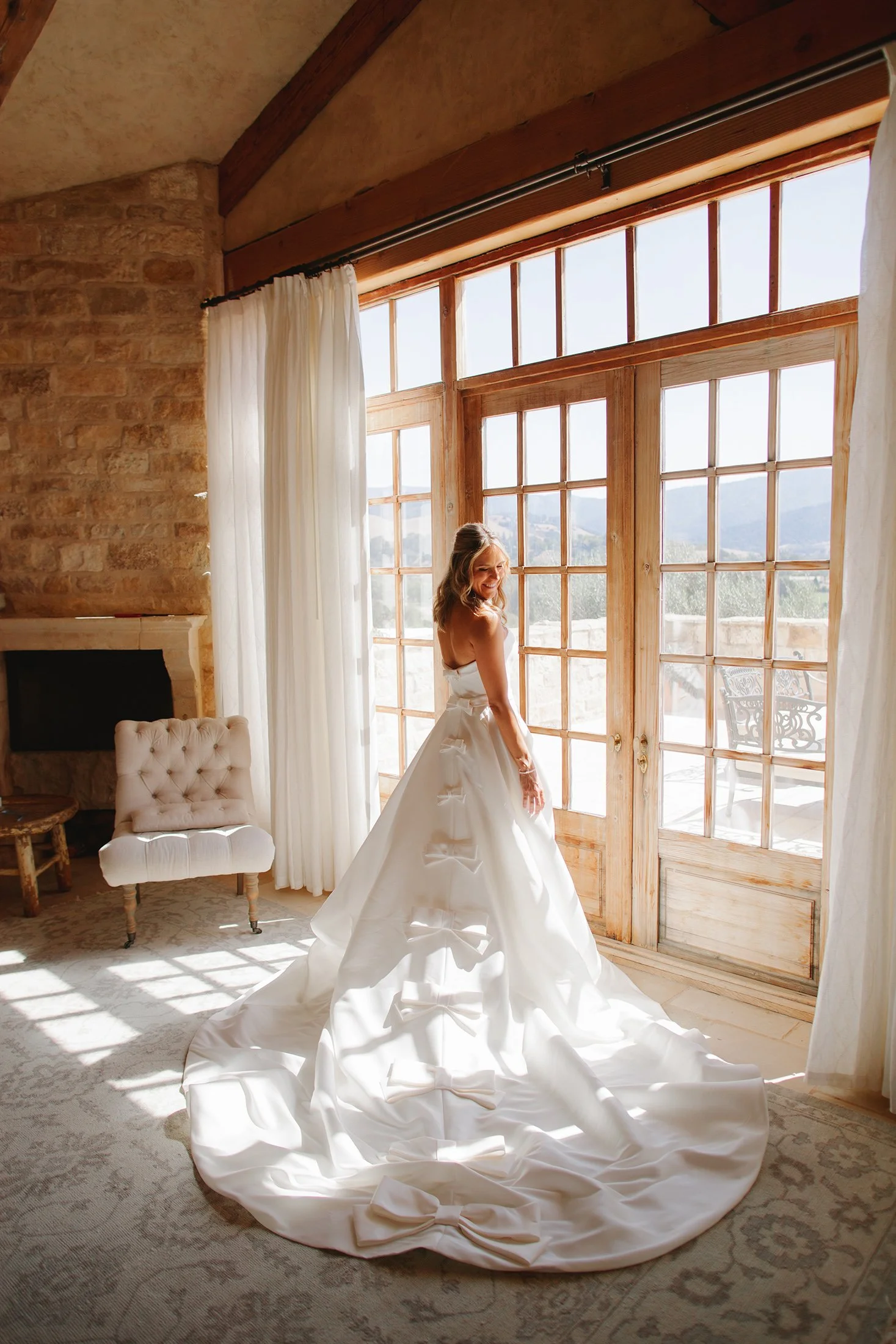 Bride in white wedding dress standing by sunlit window at Sunstone Villa, photographed by Michael & Anna Costa