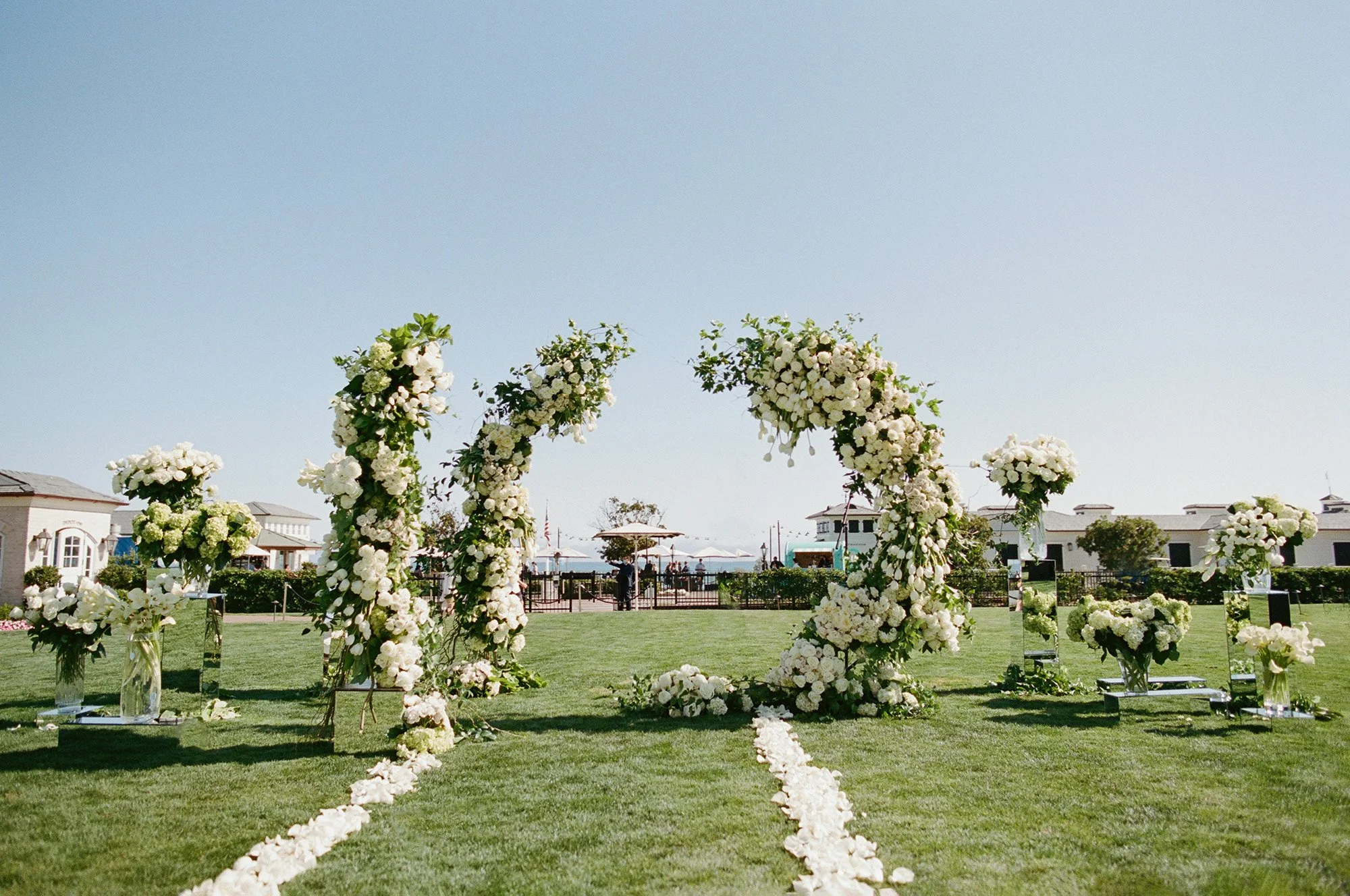 Outdoor wedding ceremony arch decorated with greenery and flowers on the lawn at Rosewood Miramar Beach, photographed by Michael & Anna Costa