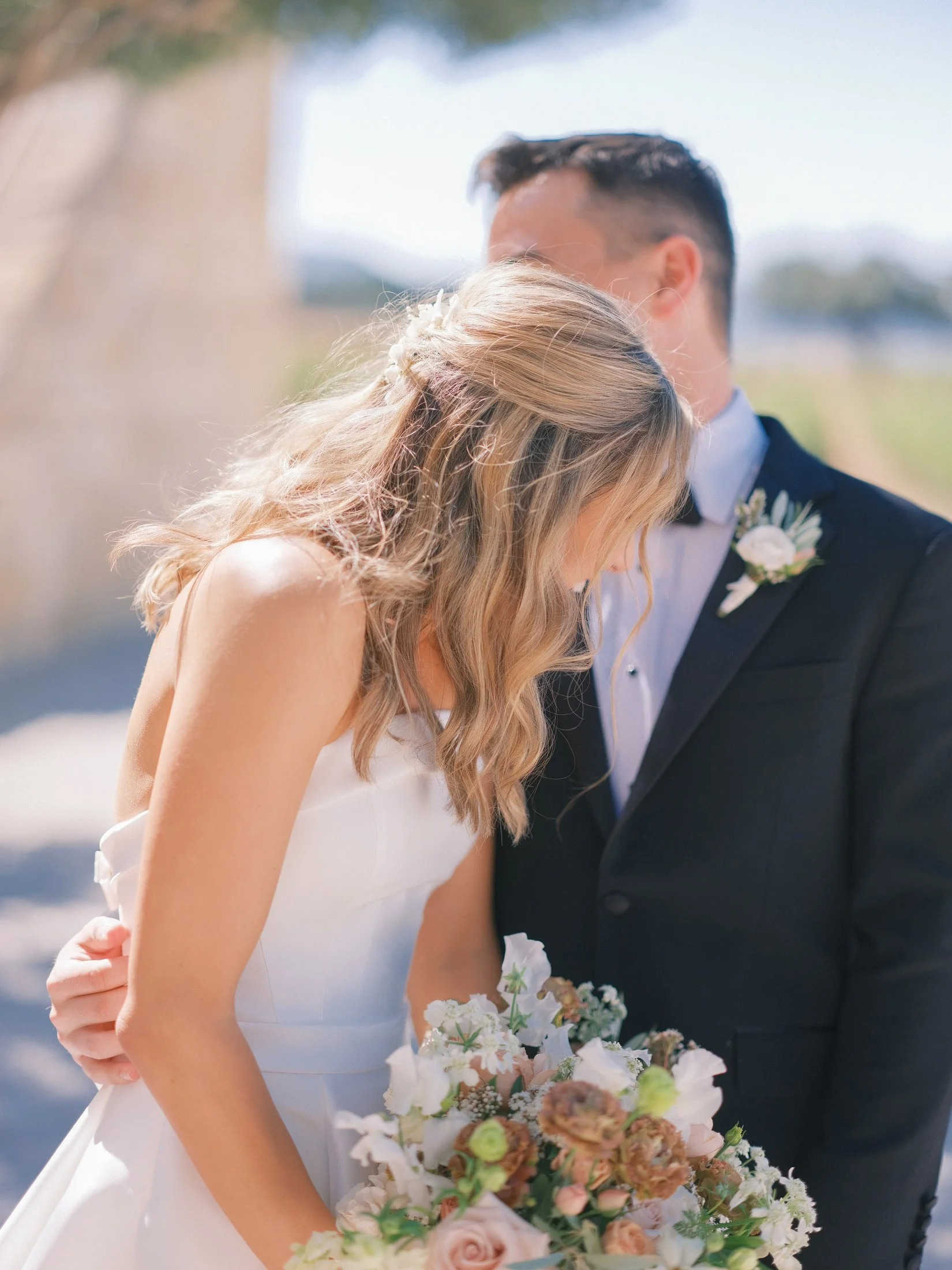 Bride and groom smiling and holding a bouquet outdoors.
