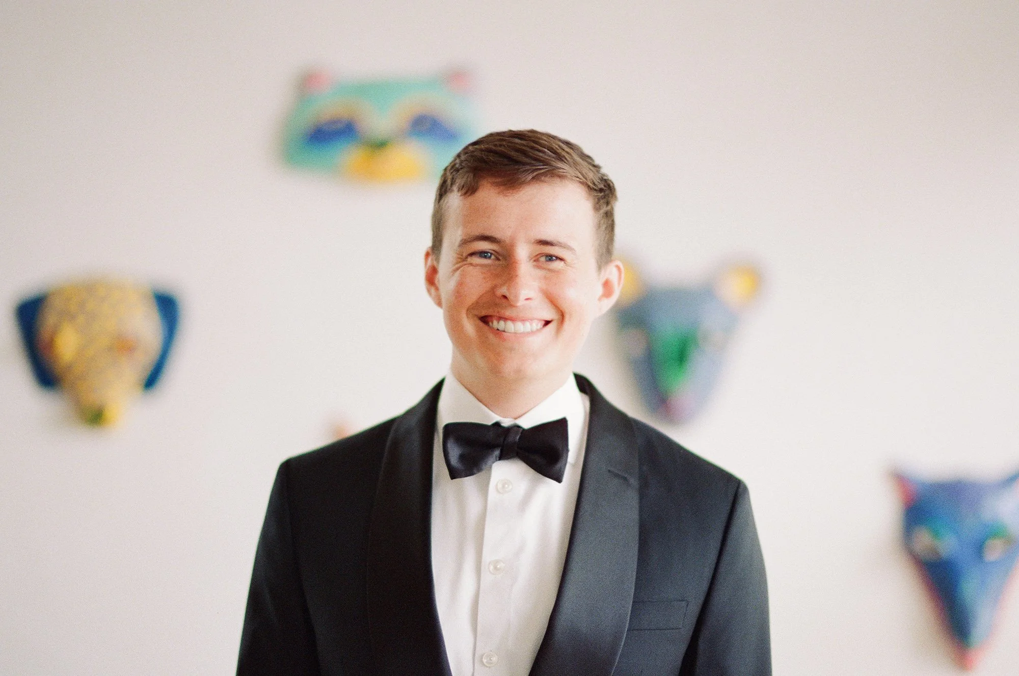 Smiling groom in a black tuxedo photographed by Michael and Anna Costa
