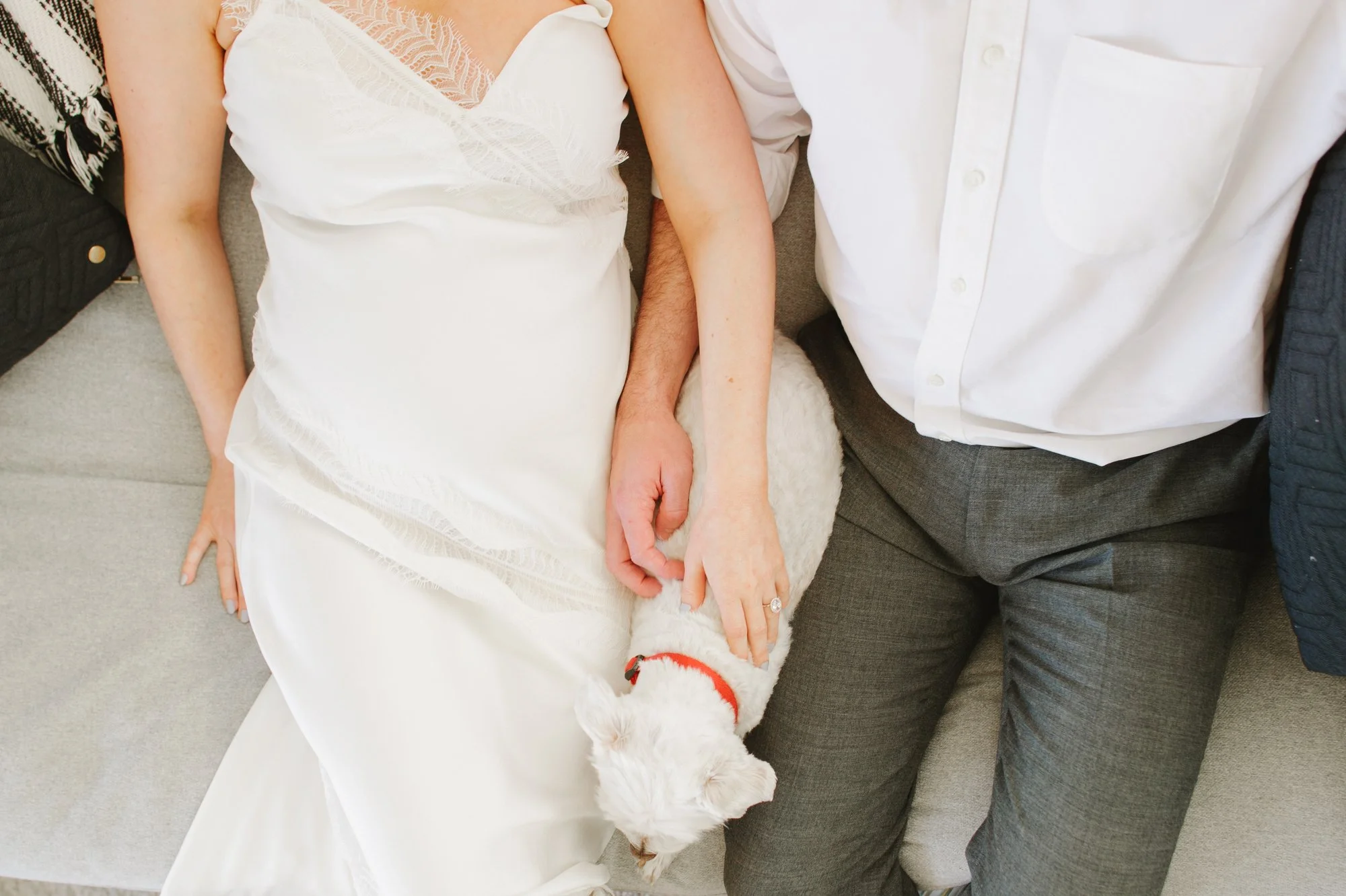 Woman in a white dress sitting next to a man, their dog resting between them.