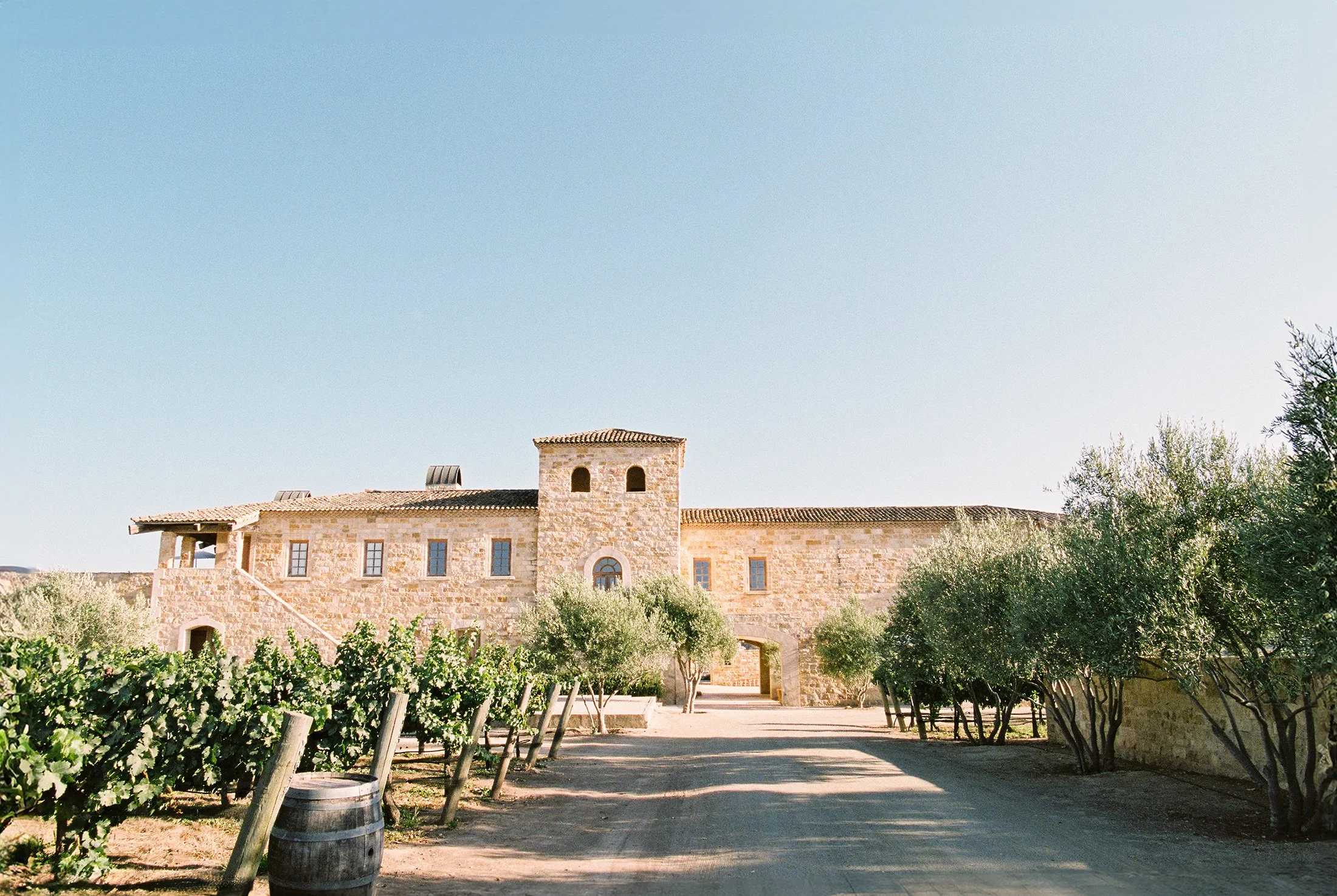 Outdoor view of a stone villa surrounded by trees and blue sky.