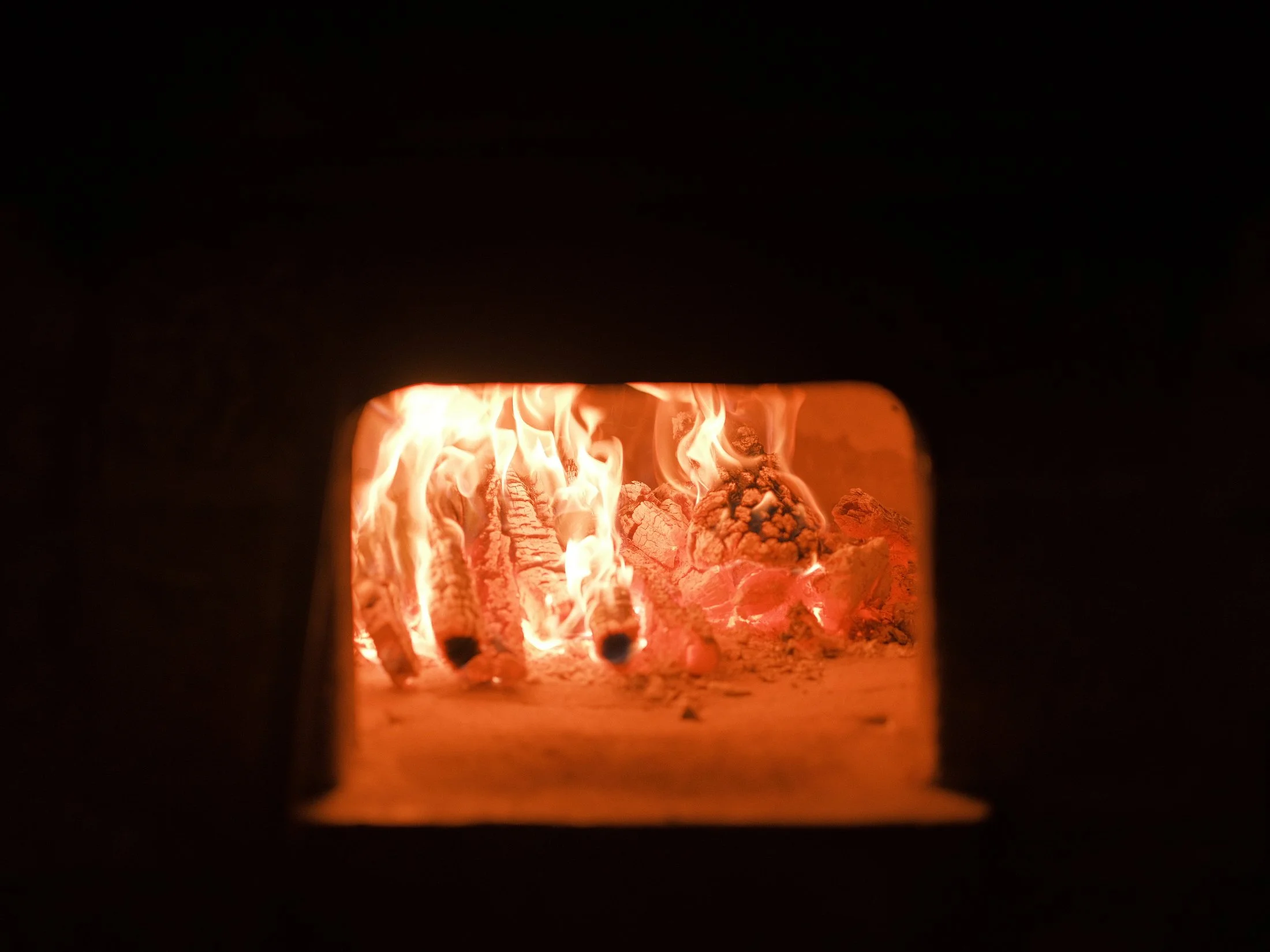 Wood-fired oven with flames glowing inside, ready for outdoor event catering.