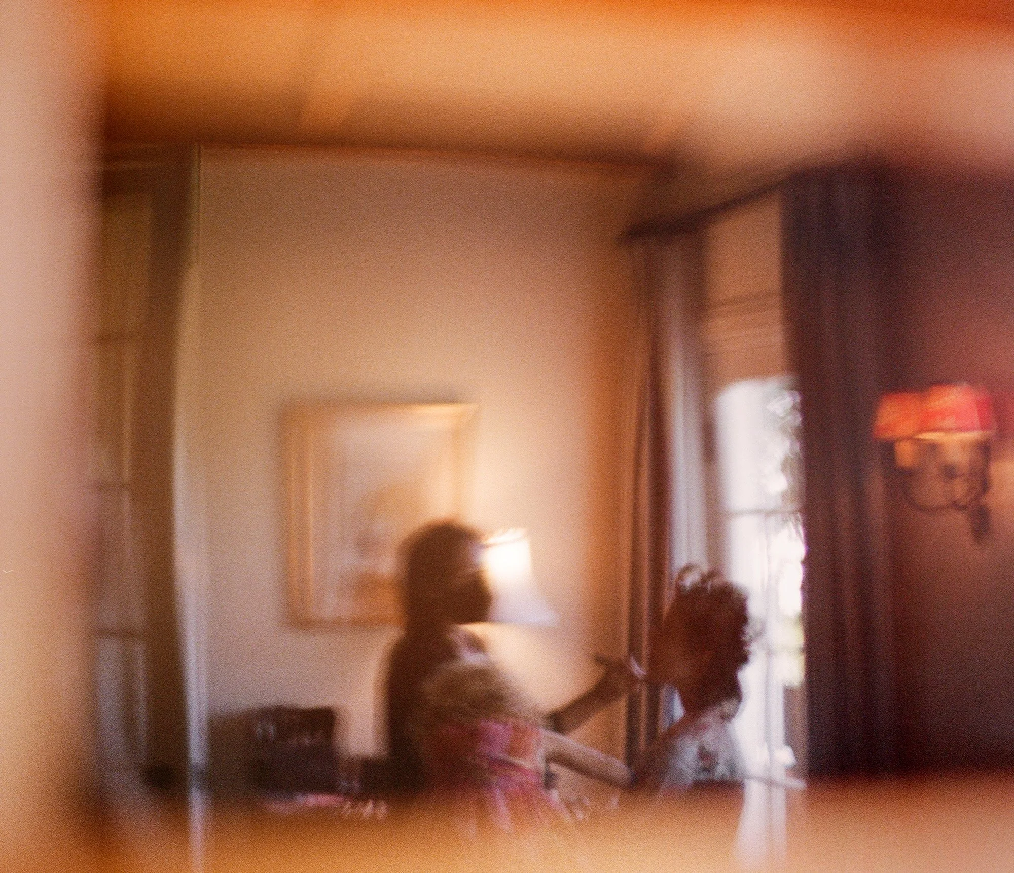 Artistic, softly focused portrait of a woman standing by a window with warm sunlight.