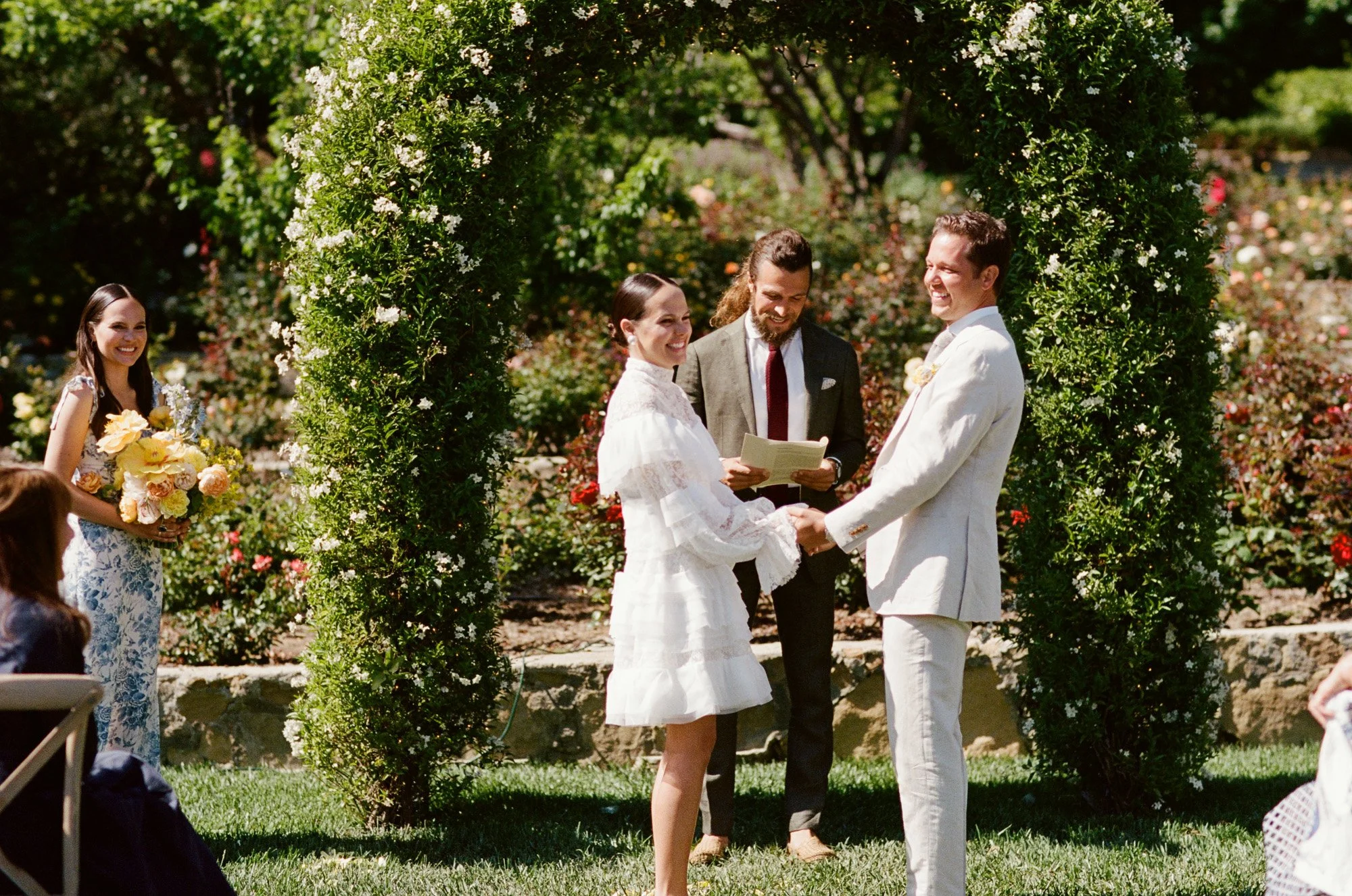 Bride and groom exchanging vows under a green archway photographed by Michael & Anna Costa