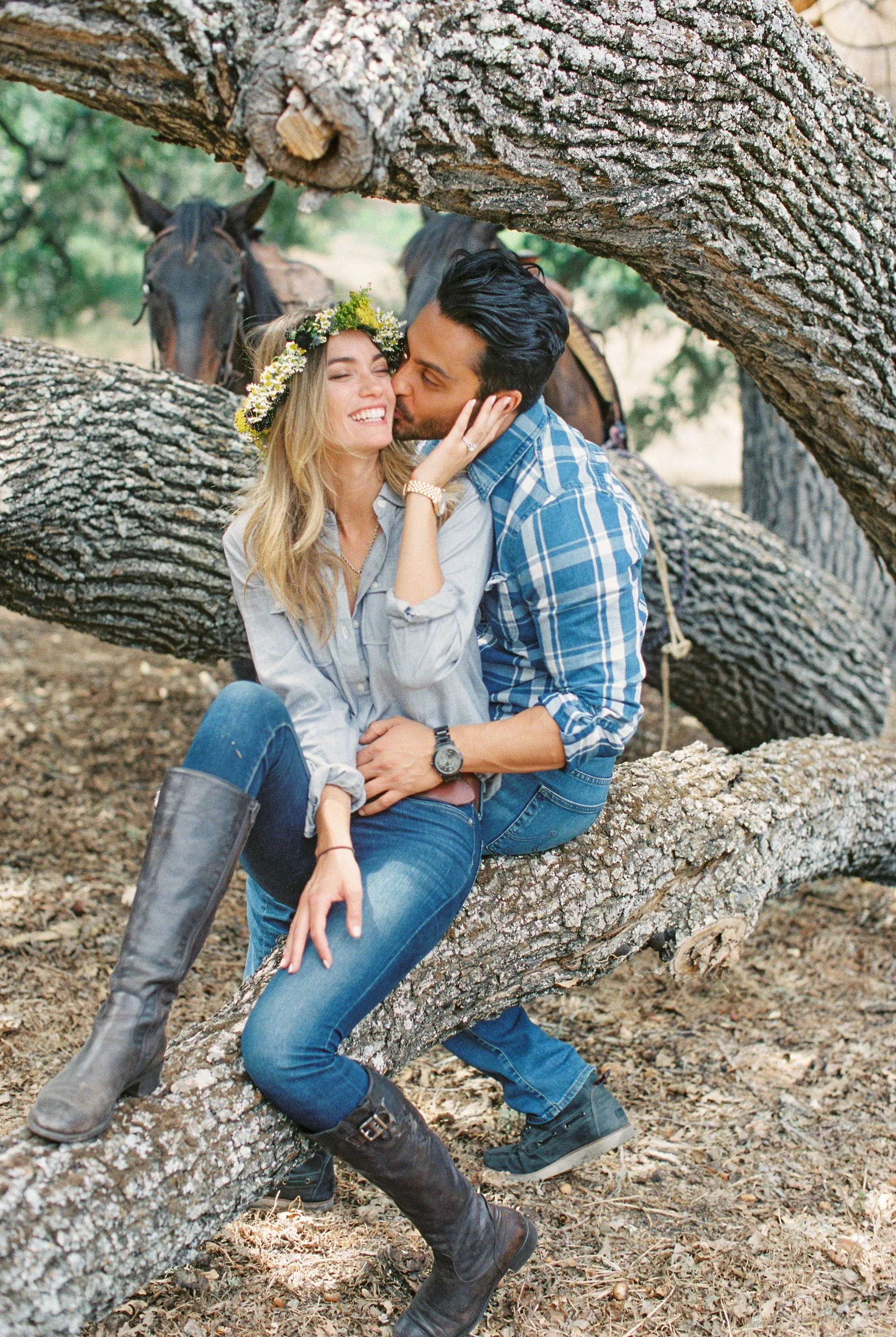 Couple sitting together on a tree branch, both wearing plaid shirts.