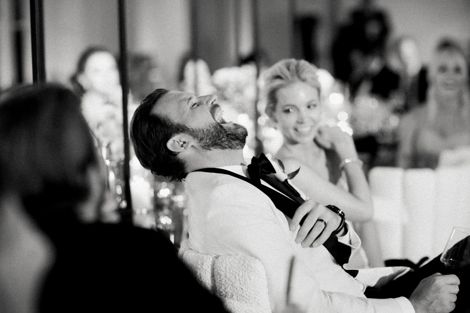 Black and white photo of groom laughing during wedding reception speeches at Rosewood Miramar Beach, photographed by Michael & Anna Costa
