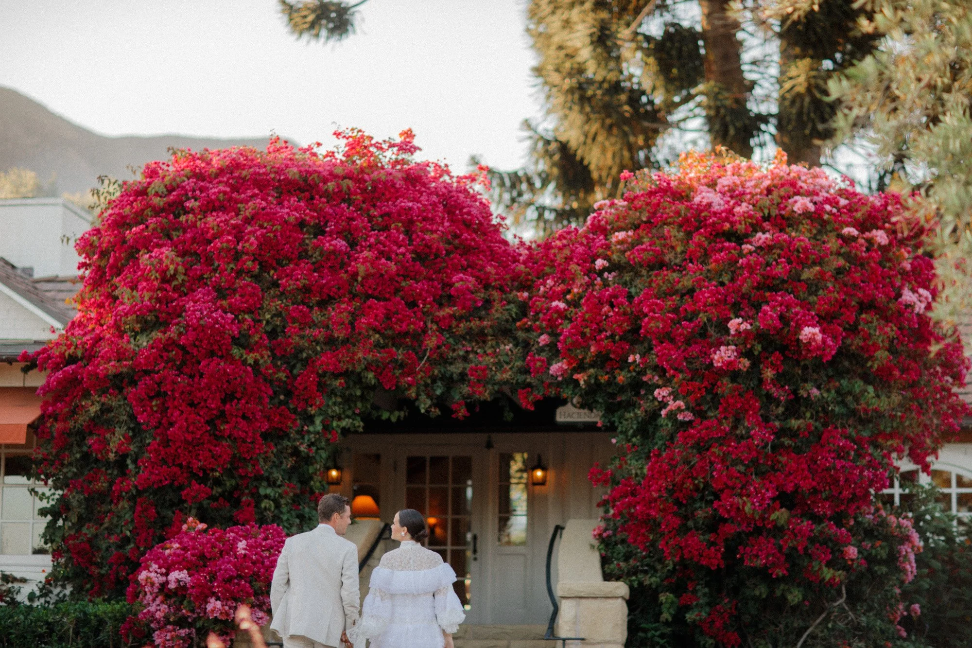 Bride and groom entering a cottage covered in vibrant pink bougainvillea at San Ysidro Ranch, photographed by Michael & Anna Costa