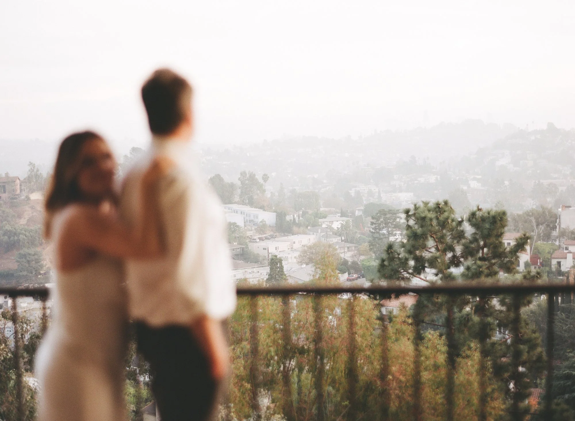 Couple standing together on a balcony, overlooking a scenic city view at sunset