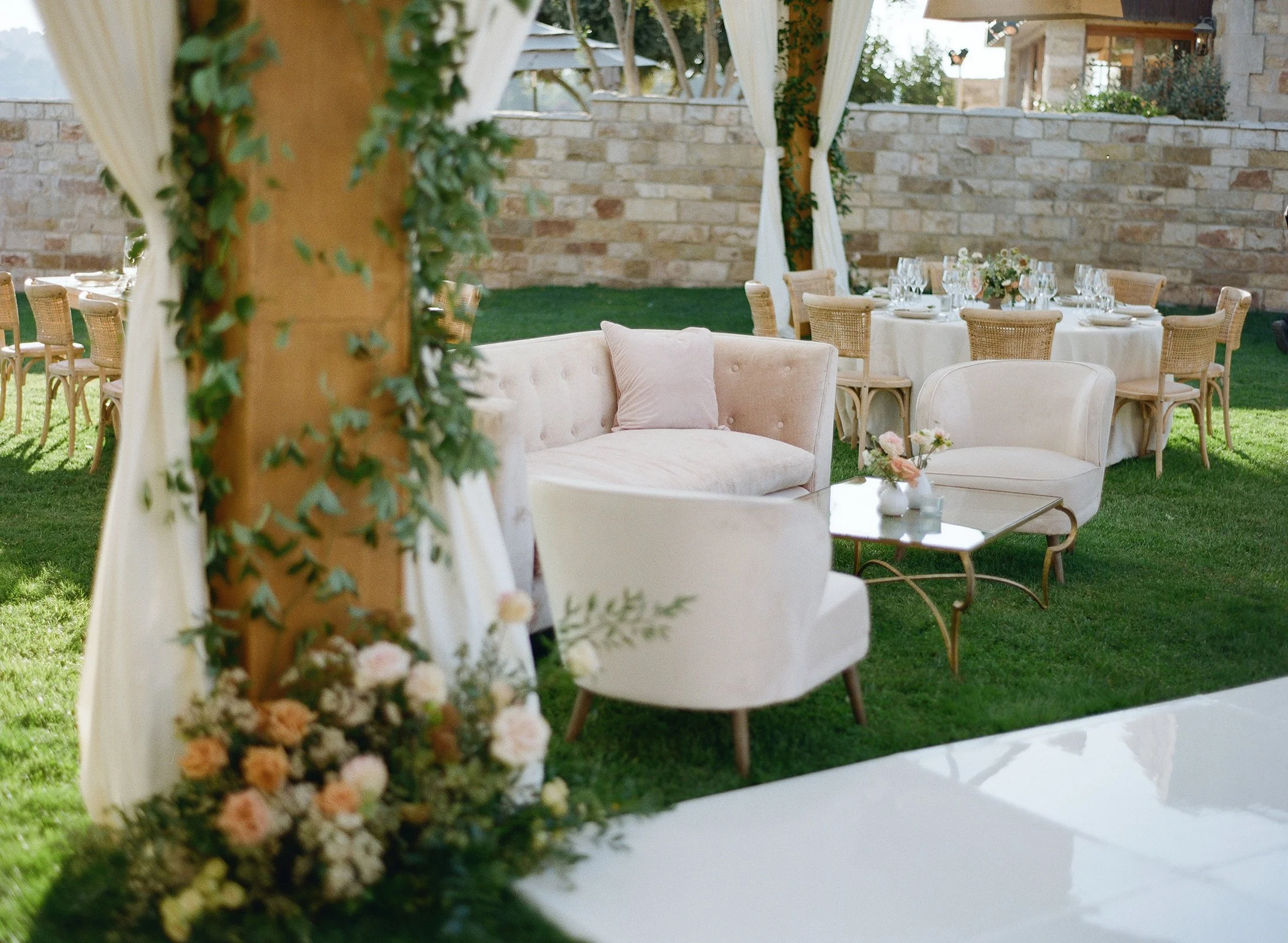 Outdoor lounge area with white sofas and floral decor at a wedding reception.