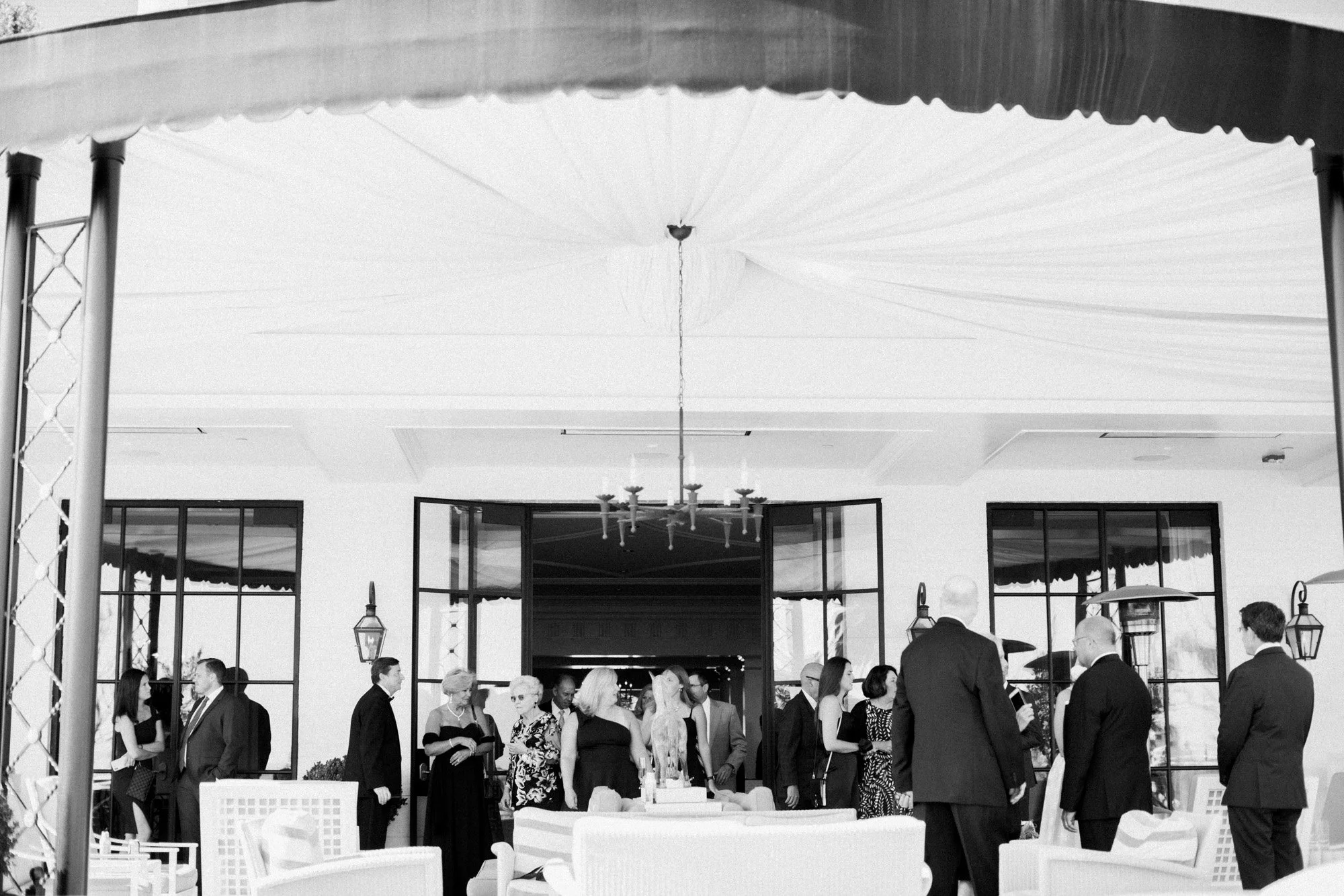 Black and white photo of guests mingling under a tent at Rosewood Miramar Beach wedding reception, photographed by Michael & Anna Costa