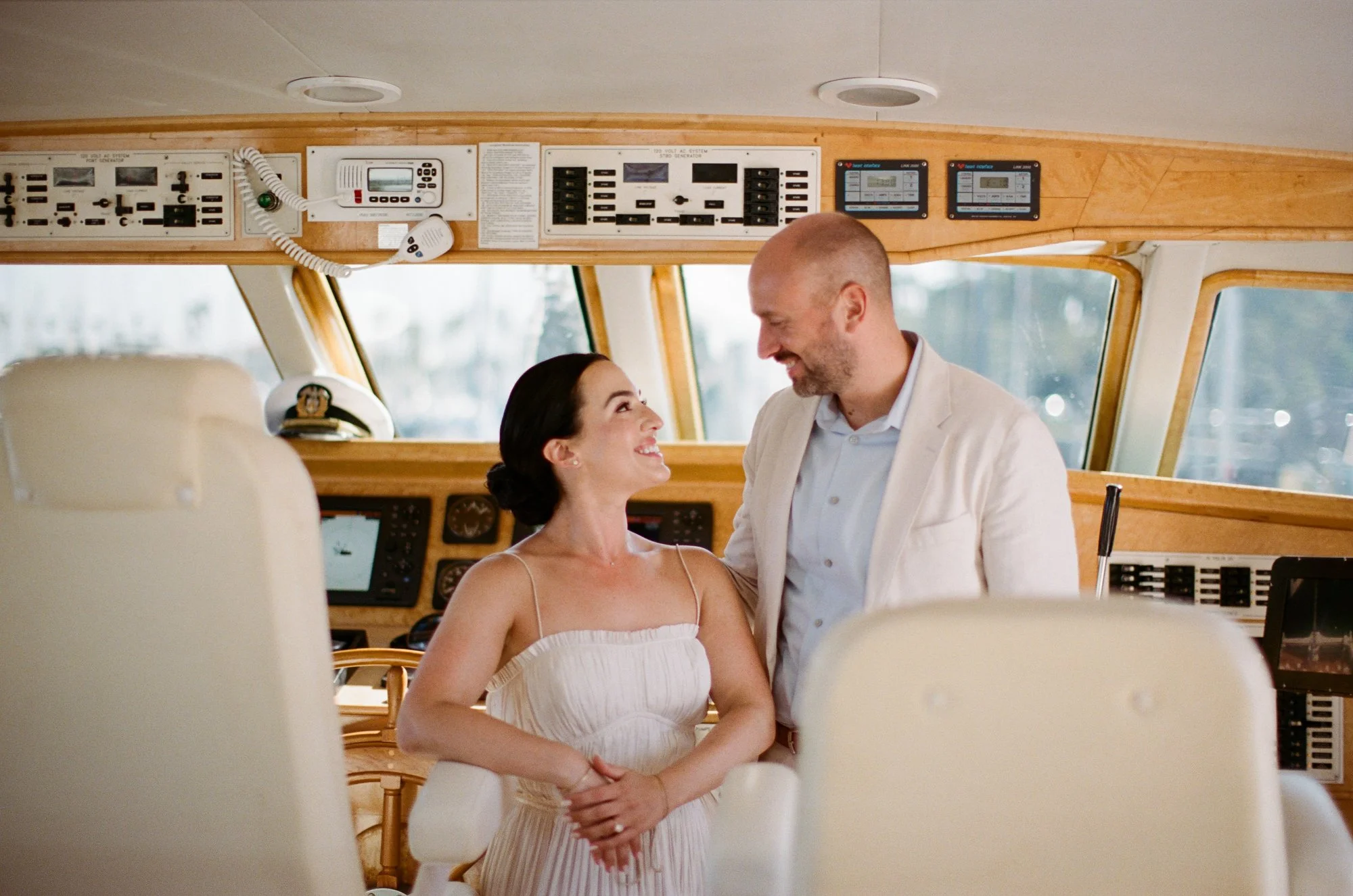 Bride and groom standing together at the yacht’s helm, smiling.