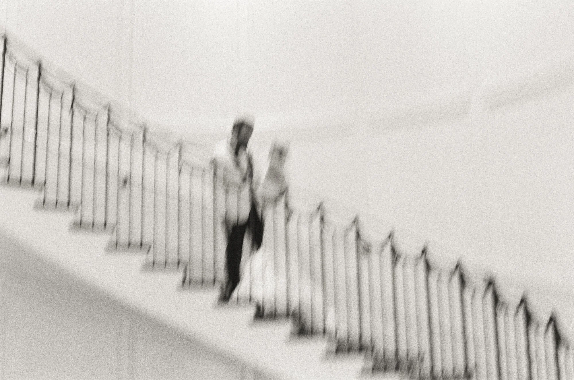 Black and white photo of bride and groom walking up a grand staircase at Rosewood Miramar Beach, photographed by Michael & Anna Costa