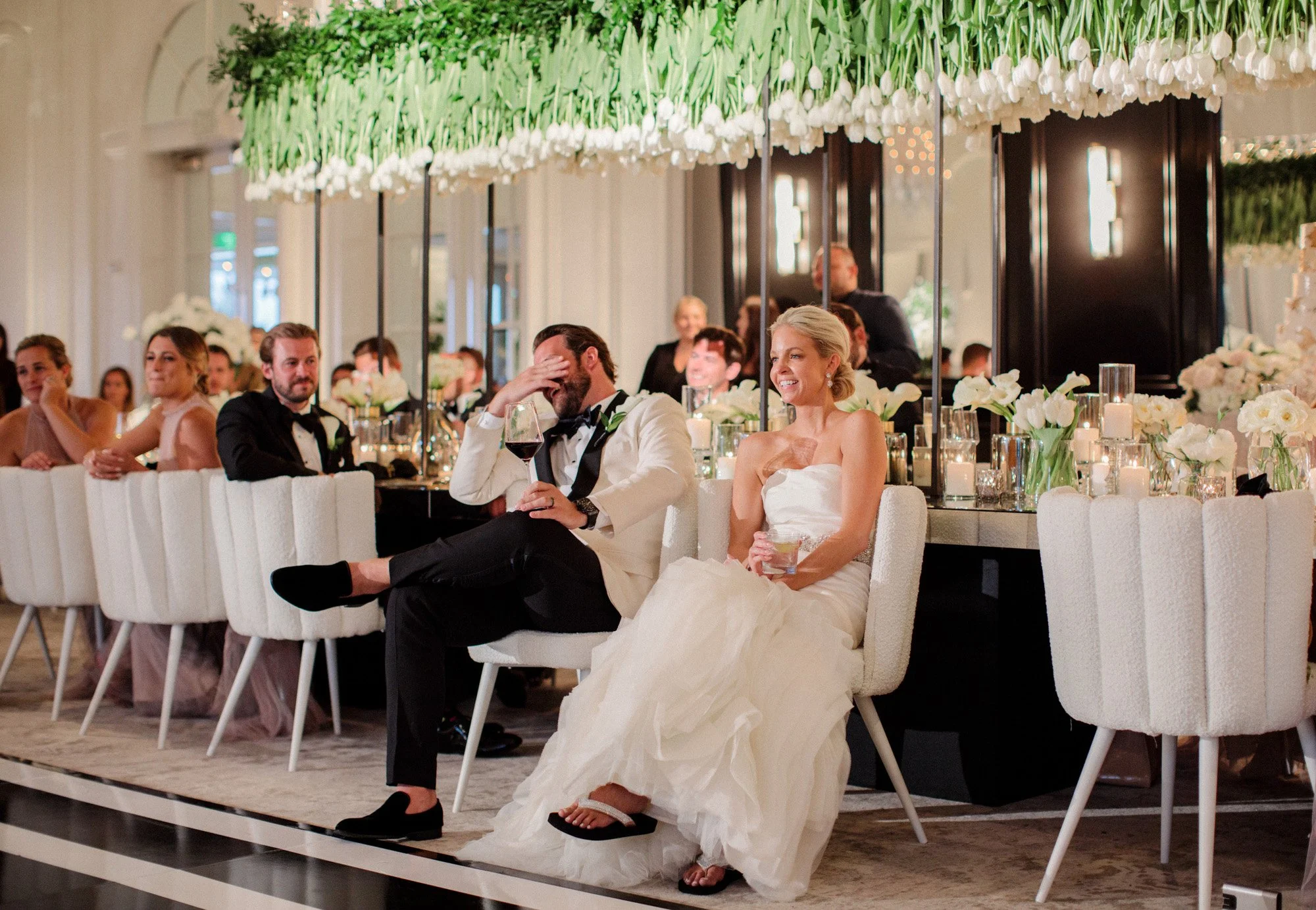 Bride and groom seated at elegant indoor wedding reception with guests at Rosewood Miramar Beach, photographed by Michael & Anna Costa