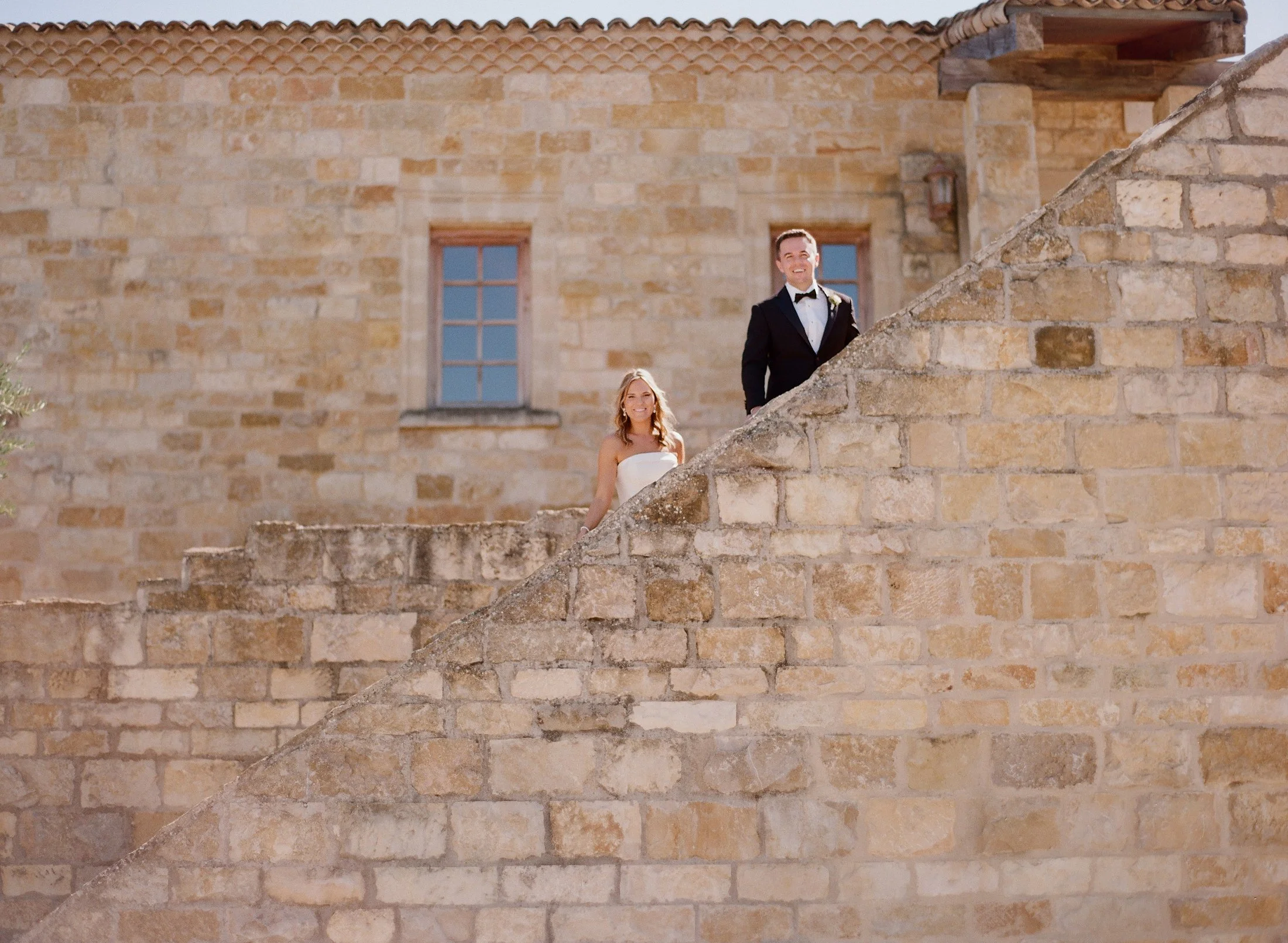 Bride and groom standing on outdoor stone steps, smiling.