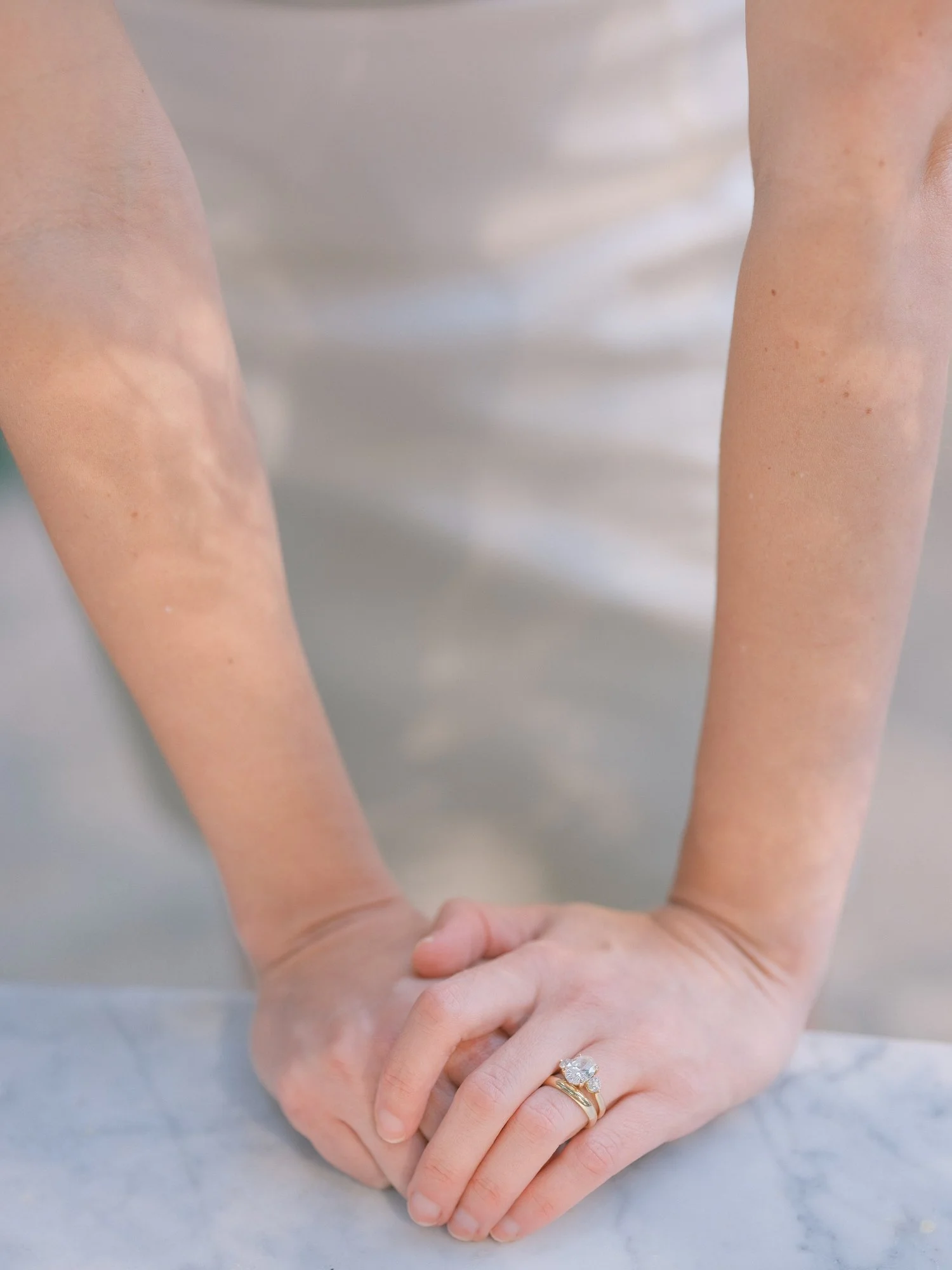 Close-up of bride and groom holding hands, sunlight filtering through leaves.