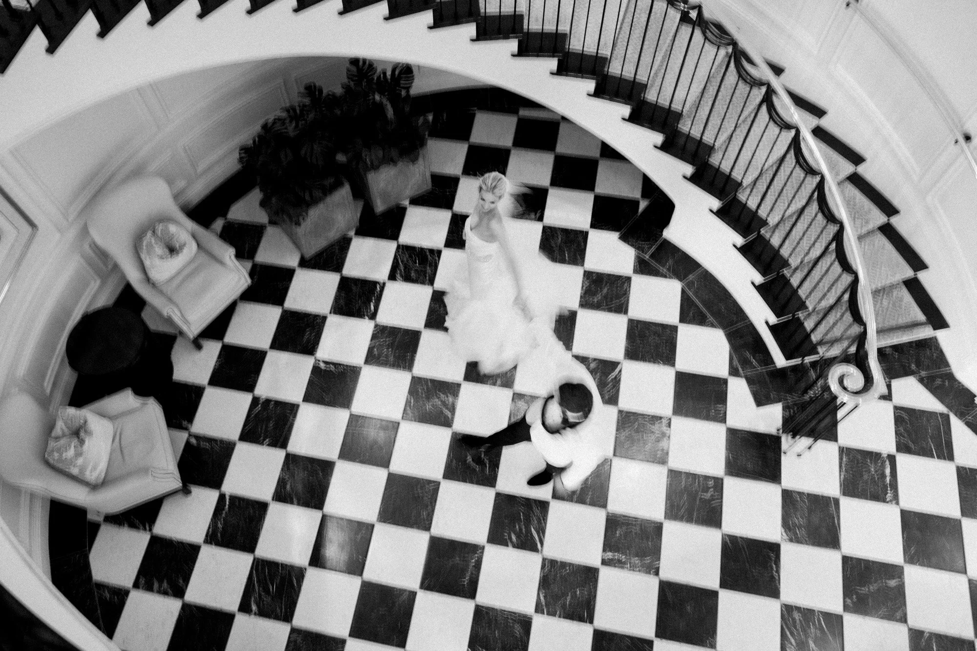 Black and white overhead photo of bride and groom dancing on a checkered floor staircase at Rosewood Miramar Beach, photographed by Michael & Anna Costa