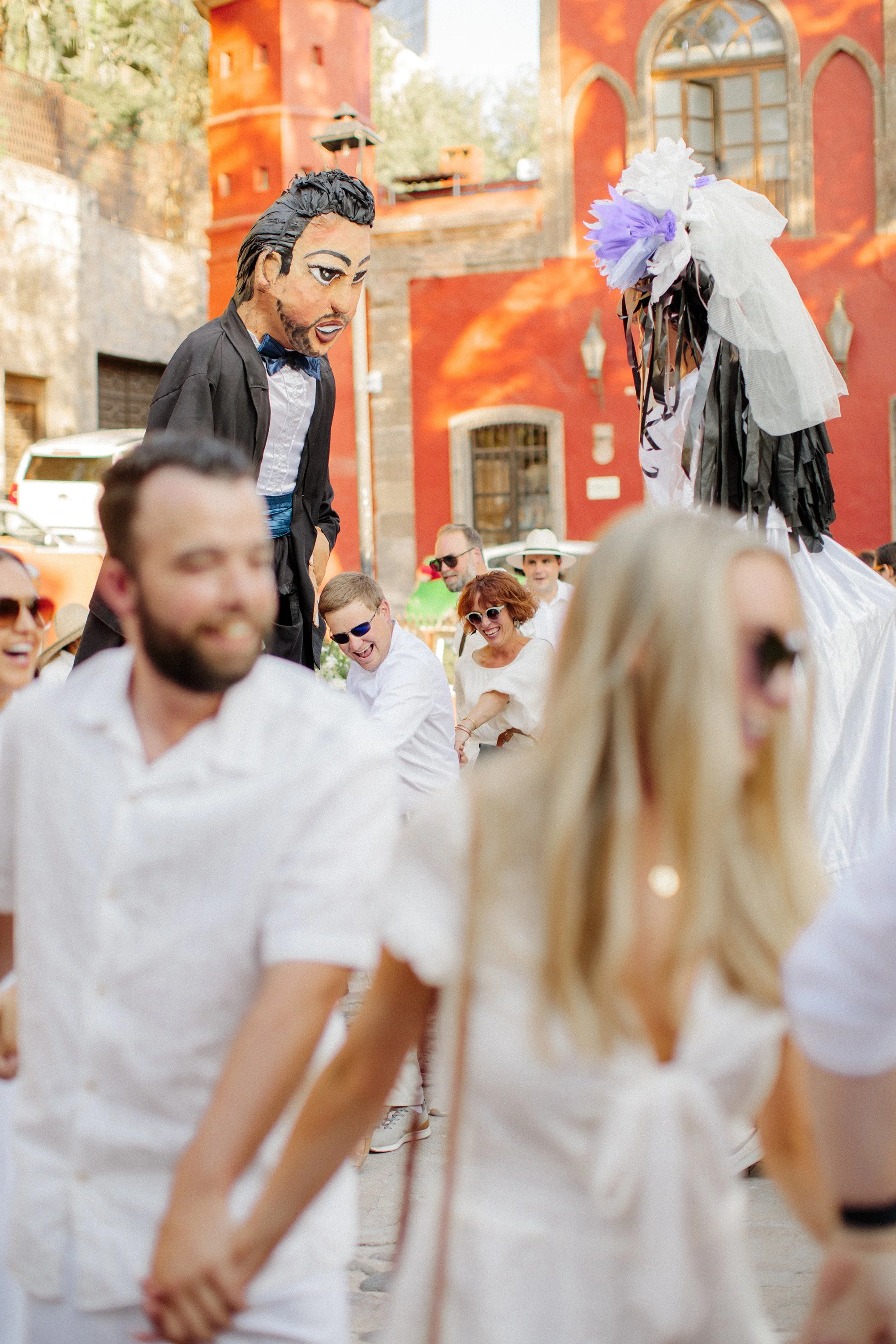Groom leading a white horse with wedding guests walking on a cobblestone street.