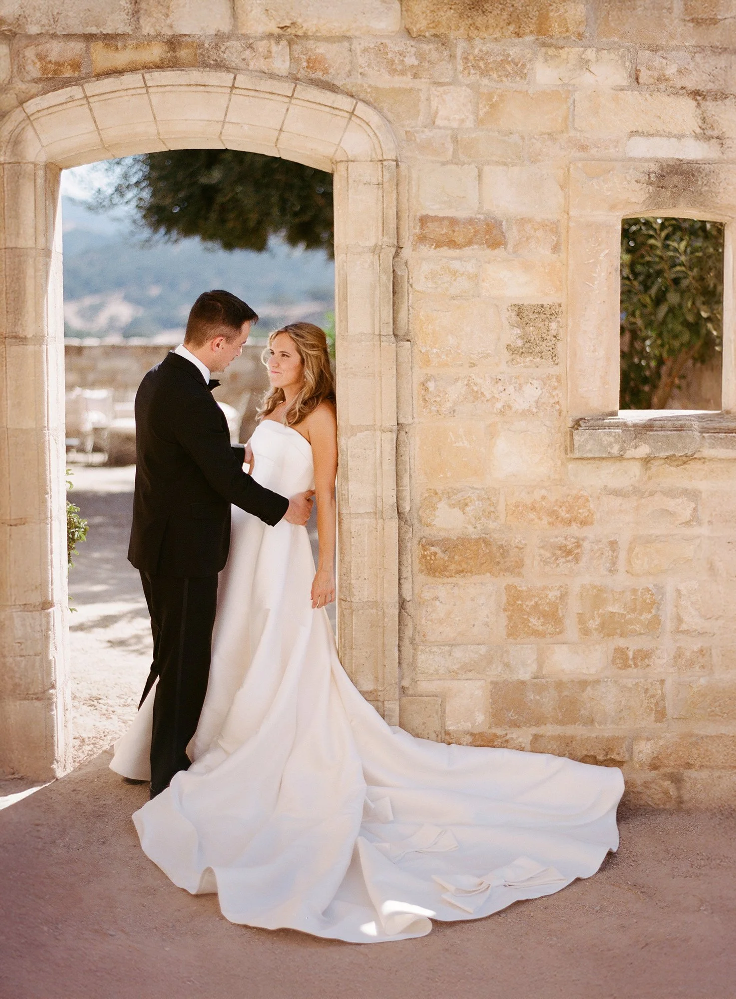 Bride and groom embracing in a stone archway.