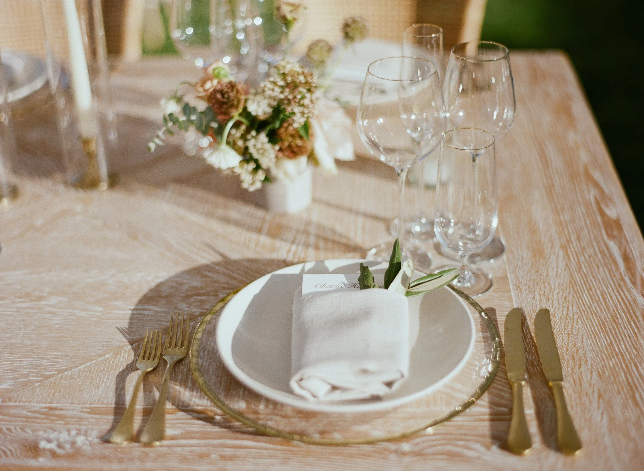 Elegant wedding table setting with gold cutlery, white napkin, and small floral centerpiece.
