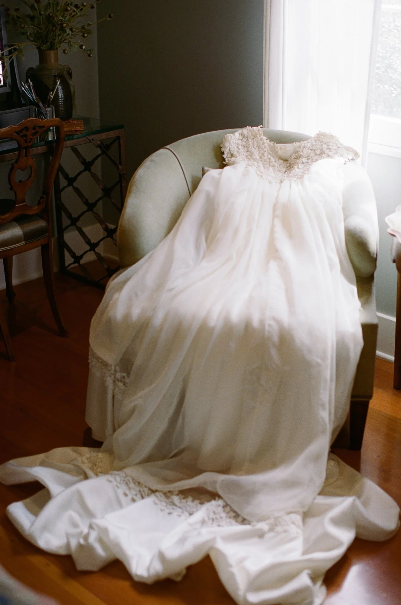 Vintage lace wedding dress draped over a chair in natural window light.