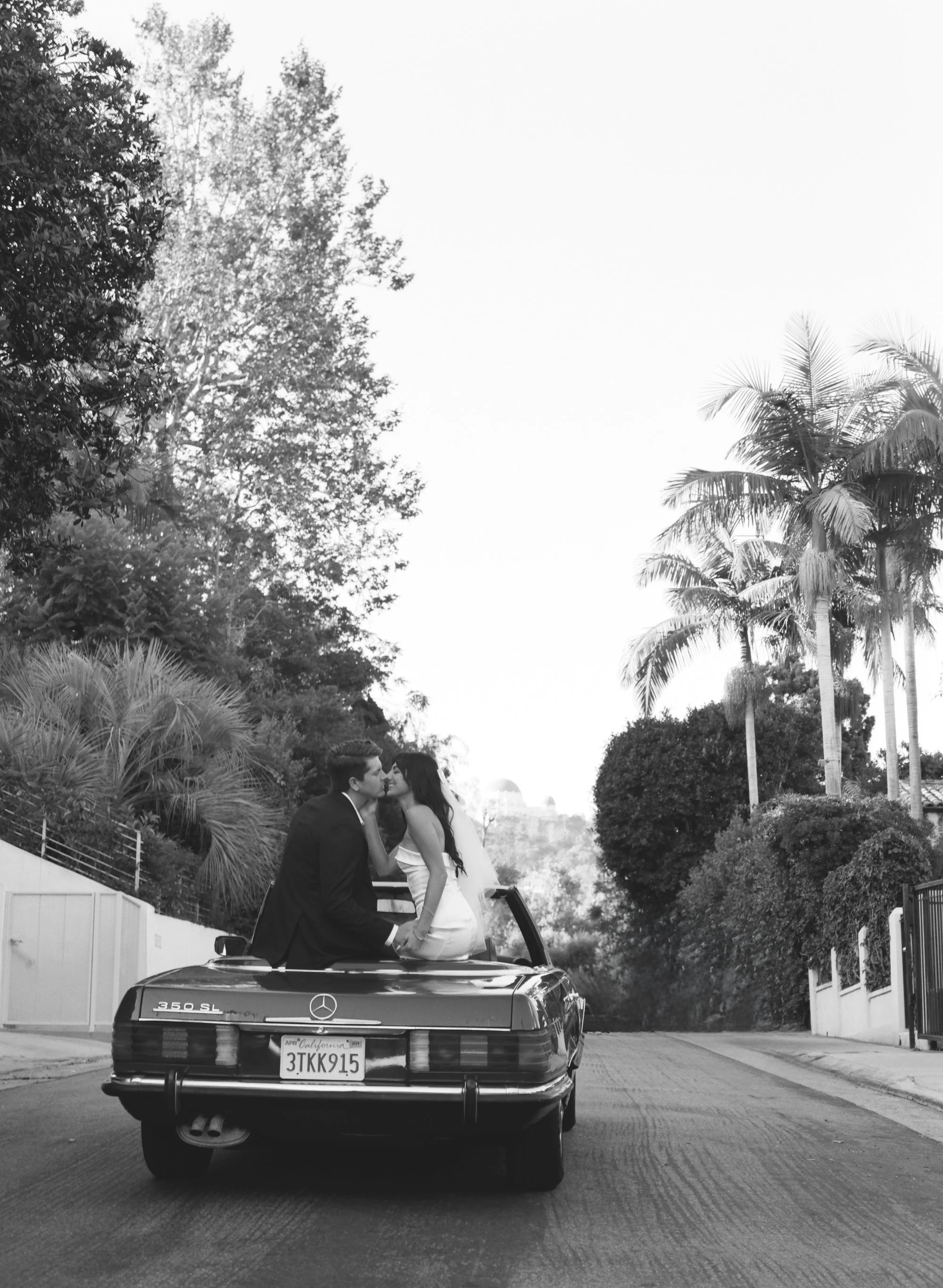 Black and white photo of couple in a vintage car, viewed from behind.