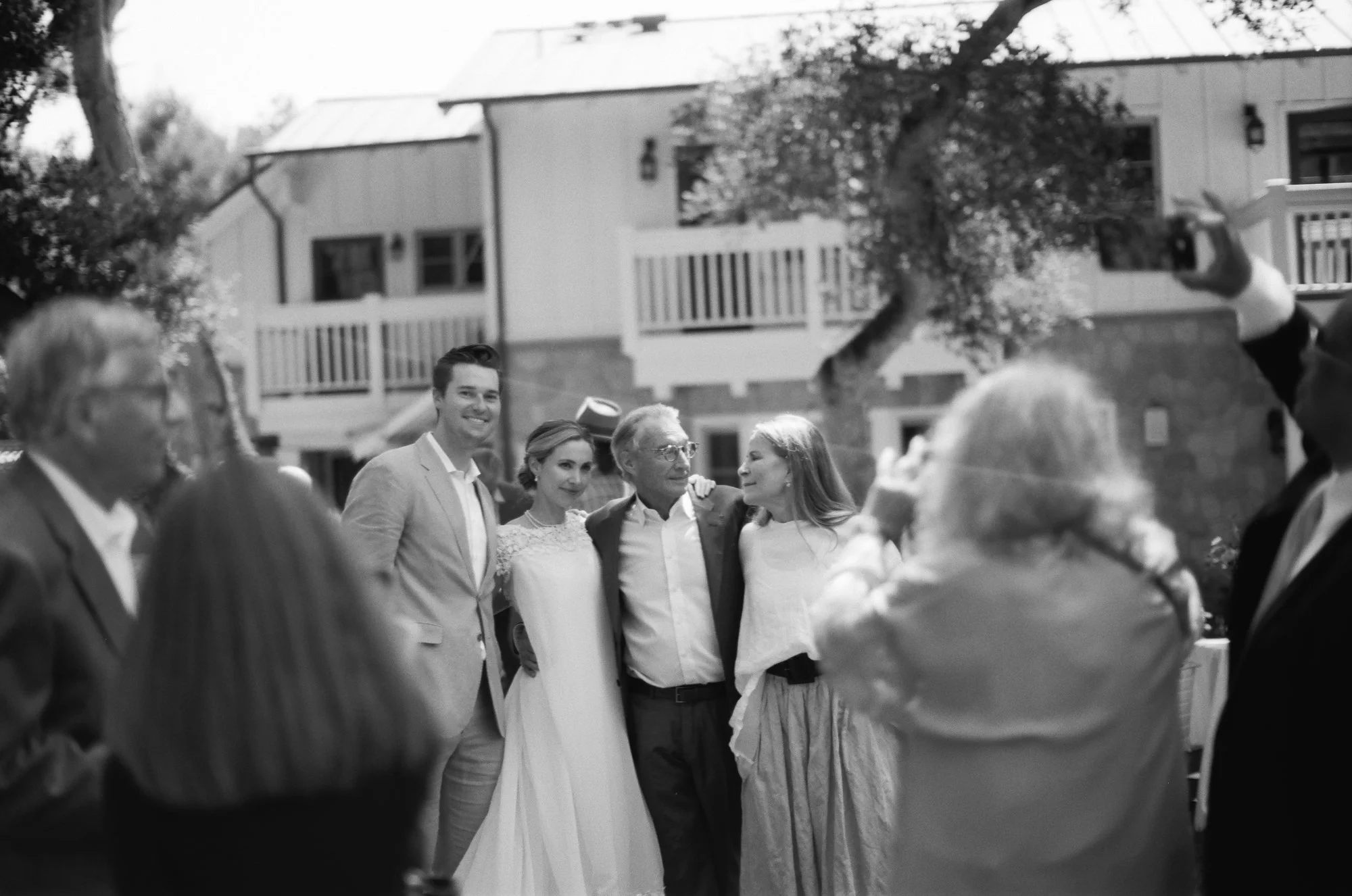 Black and white candid photo of wedding guests gathered outdoors.