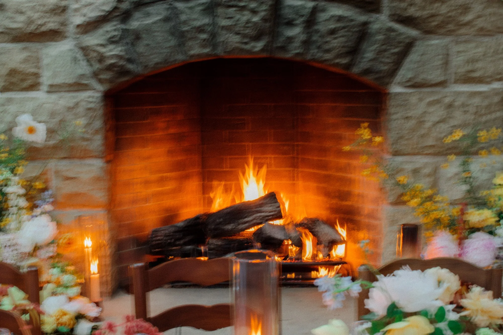 Stone fireplace with a burning fire and floral arrangements at San Ysidro Ranch wedding, photographed by Michael & Anna Costa