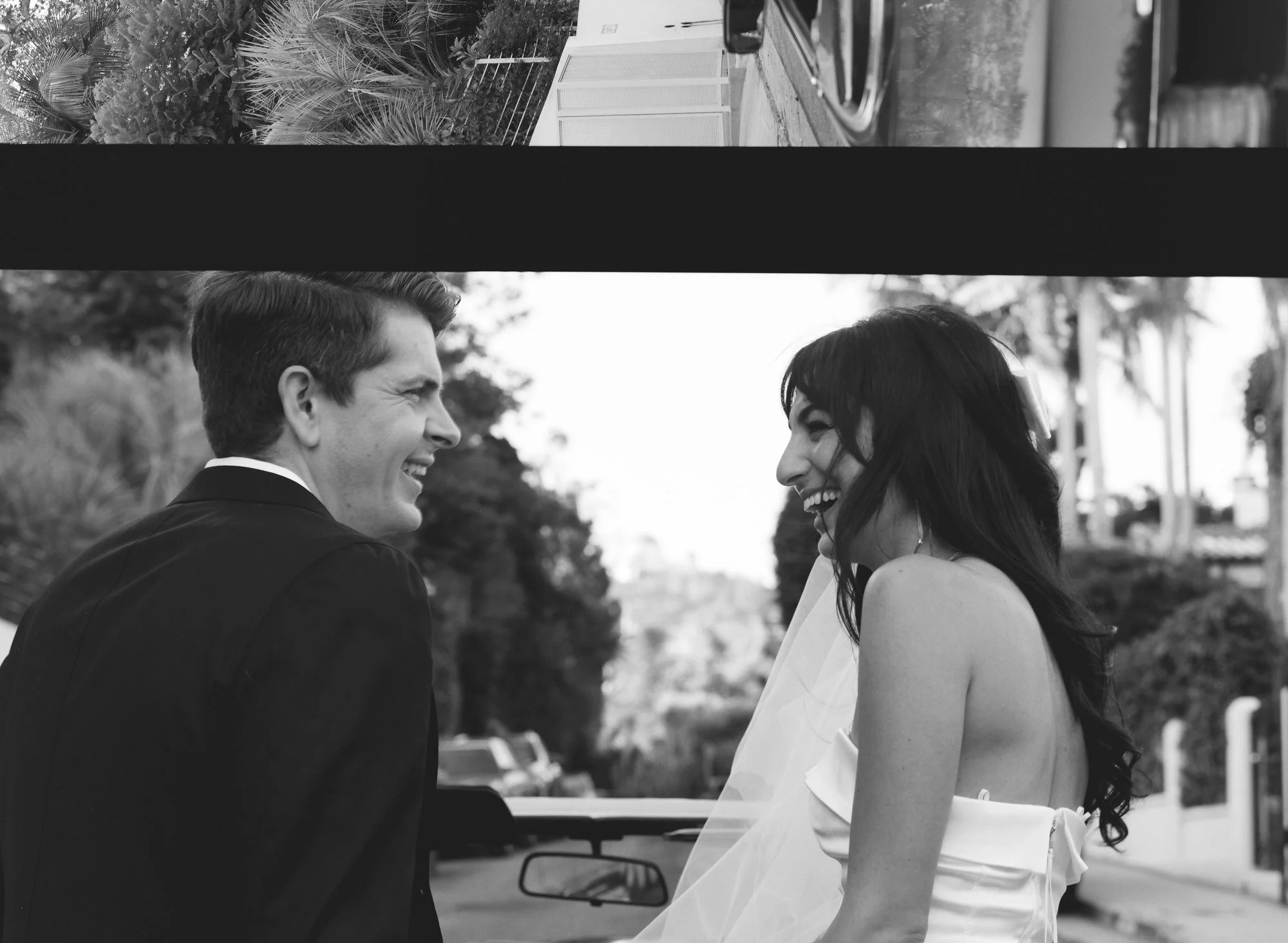 Black and white photo of couple standing together outdoors, bride in a white dress.
