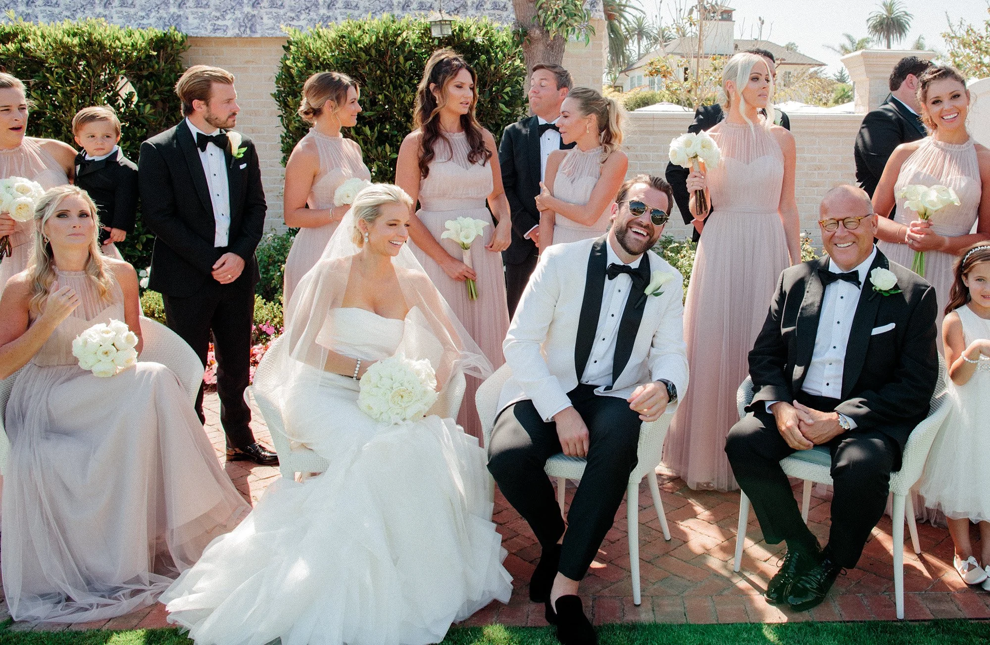 Bride and groom seated with wedding party and family outdoors at Rosewood Miramar Beach, photographed by Michael & Anna Costa
