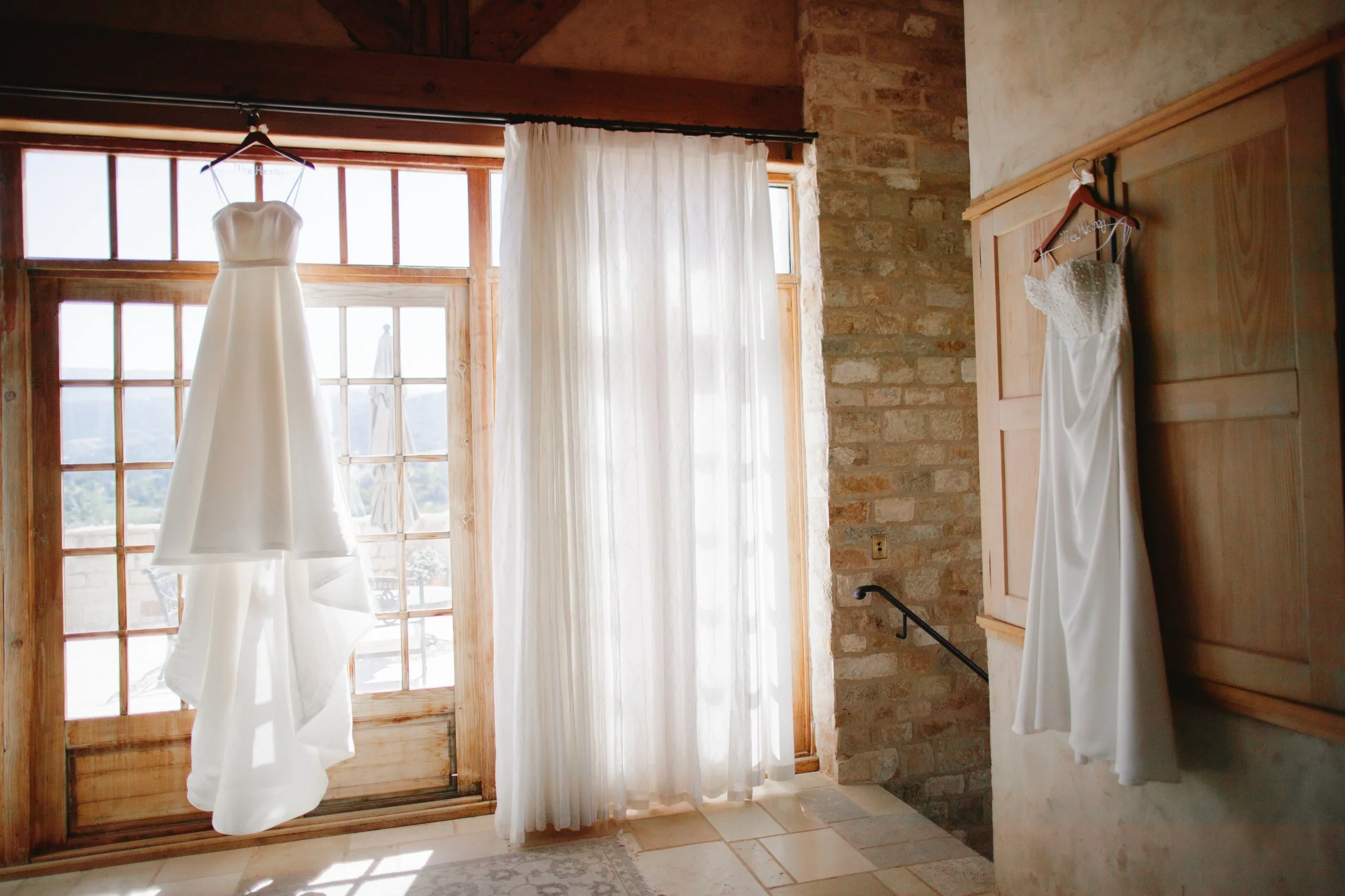 Wedding dress hanging in sunlit window of bridal suite at Sunstone Villa, photographed by Michael & Anna Costa