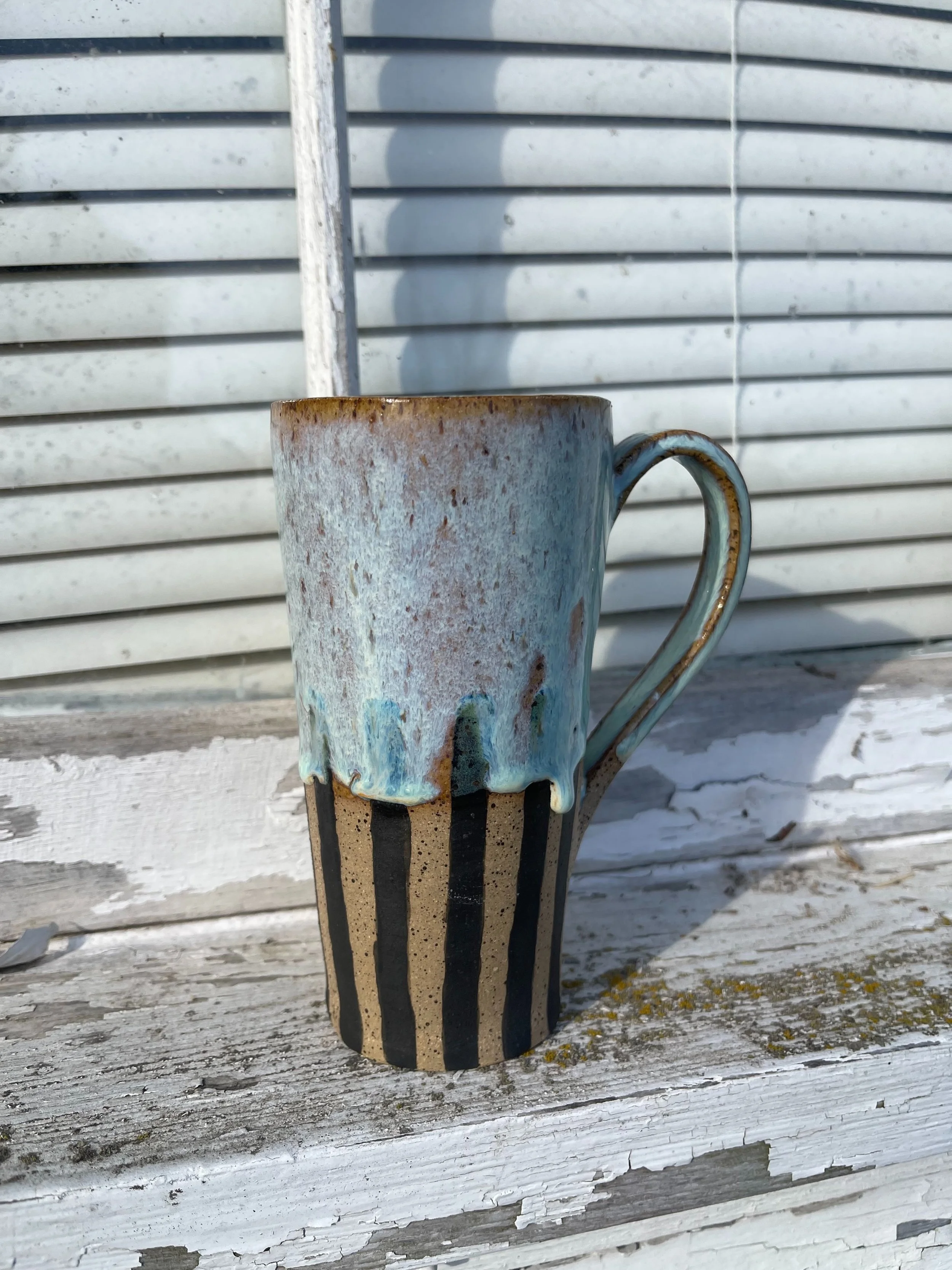 Tall Striped Ceramic Mug with Blue Drip Glaze | Handmade by Stray Cat Studios
This tall handmade ceramic mug features bold black stripes and icy blue glaze drips. A gothic-meets-whimsical showpiece—crafted for the curious and caffeine-obsessed.