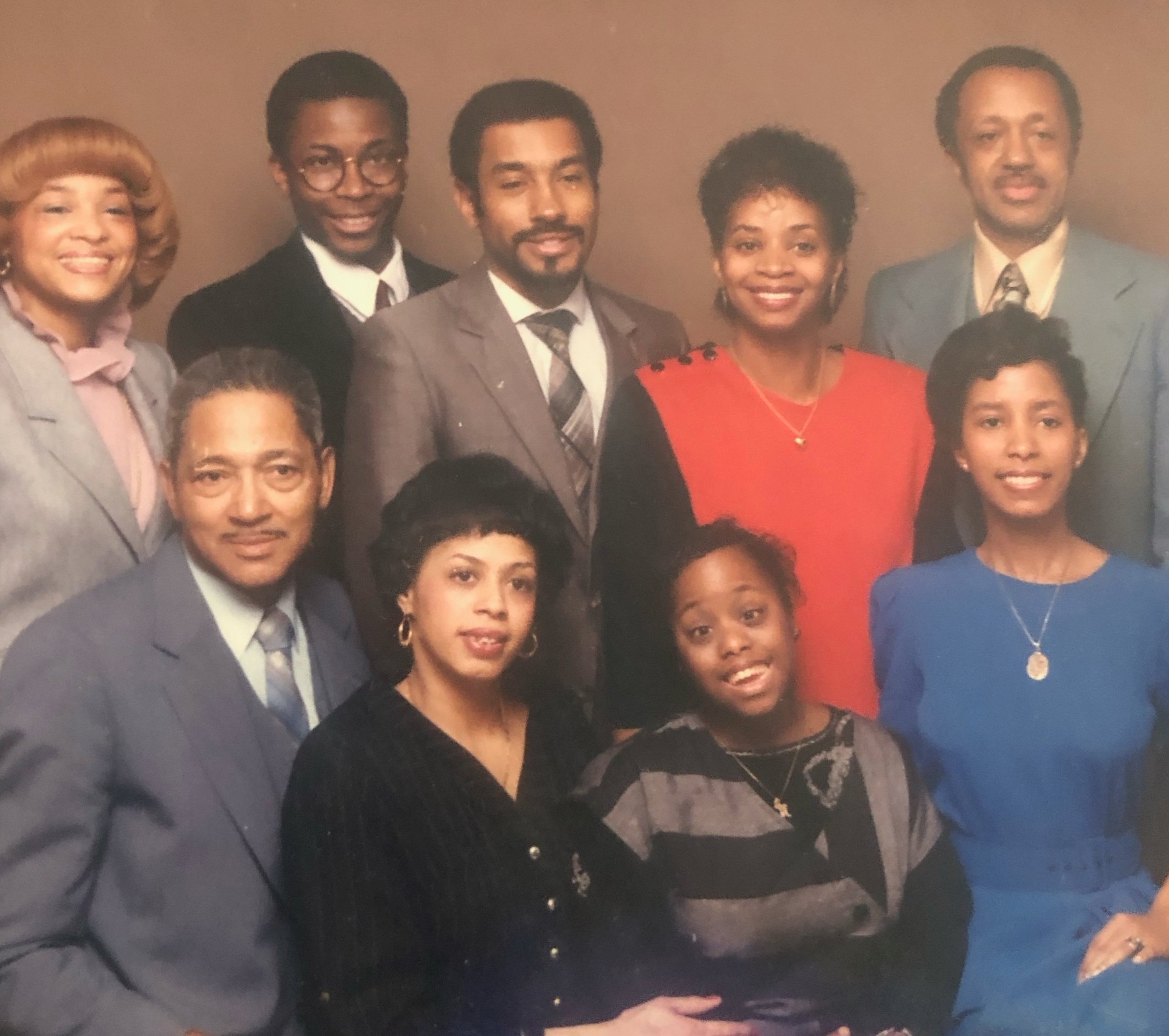 Group portrait of ten people, five men and five women, dressed in formal business attire, standing and sitting together against a plain background.