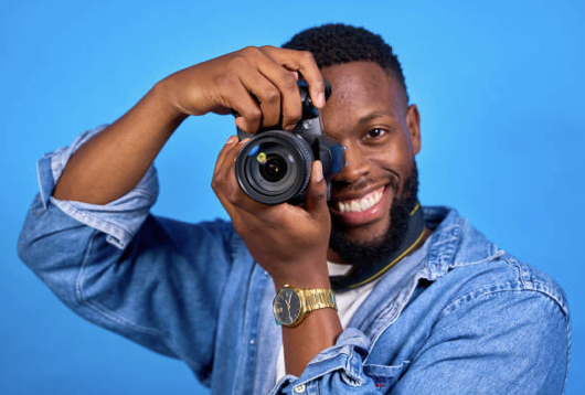 Man smiling while holding a camera against a blue background.