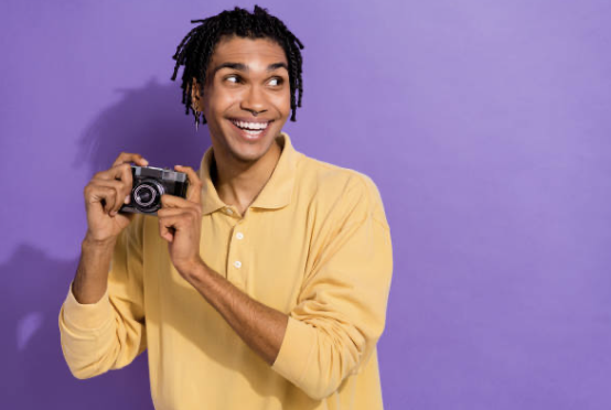 Smiling person in yellow shirt holding vintage camera against purple background